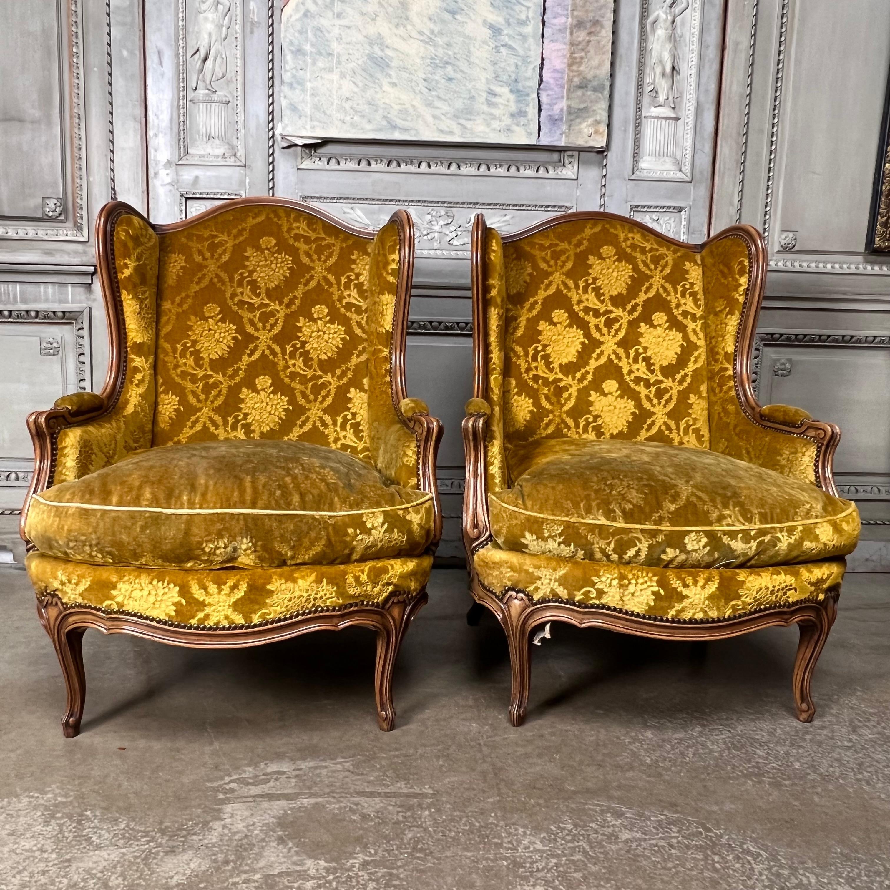 A large pair of French carved walnut Louis XV style wingback bergere.  
These comfortable chairs have a nice patina and are in good contition They are a large scale and will be comfortable for a tall person.  The fabric is old, but could be used. 