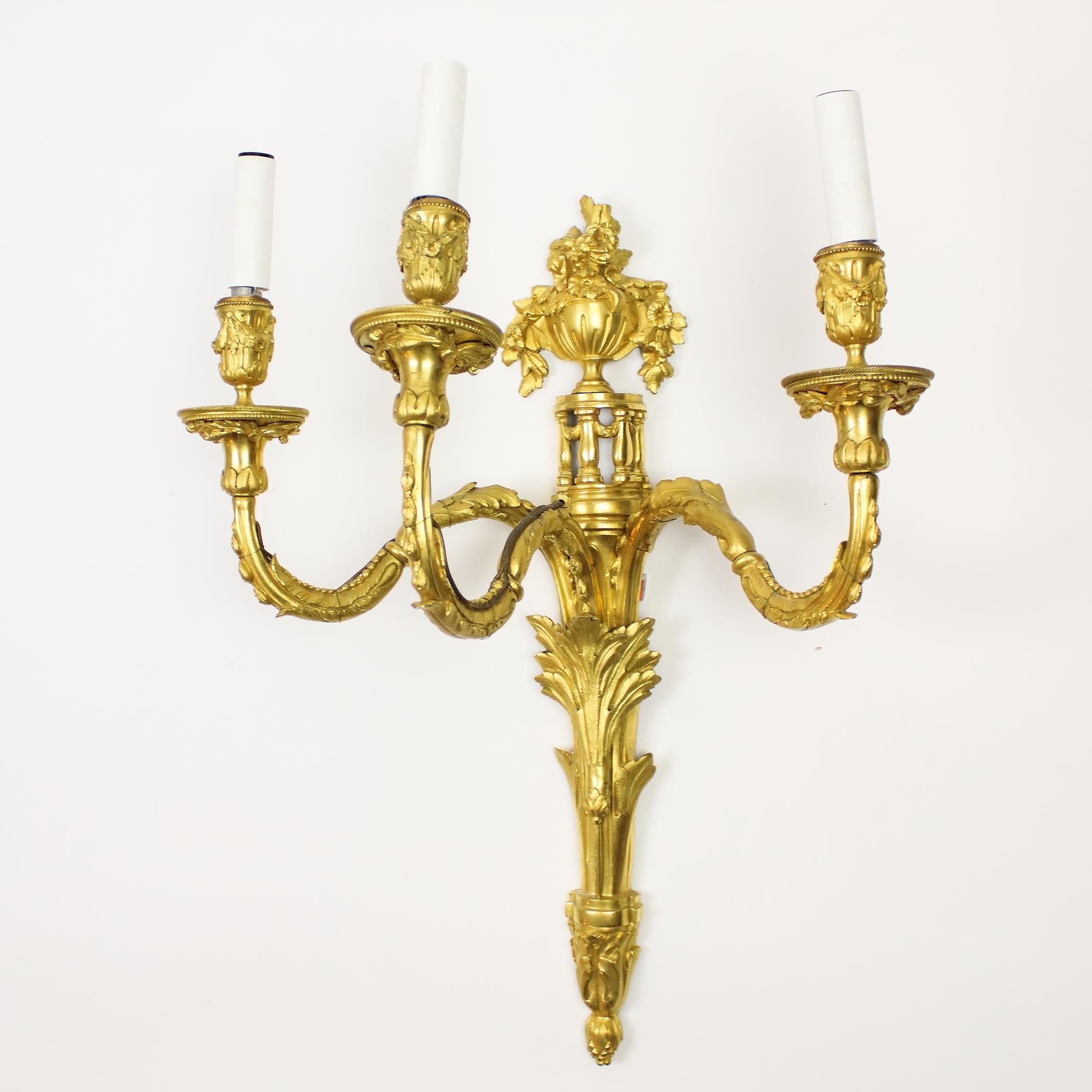 Large pair of French Louis XVI gilt bronze three-light sconces or wall lights

A pair of 19th century gilt bronze wall-lights or sconces, each with a foliage ornamented back plate surmounted by a pierced baluster gallery, supporting a neoclassical