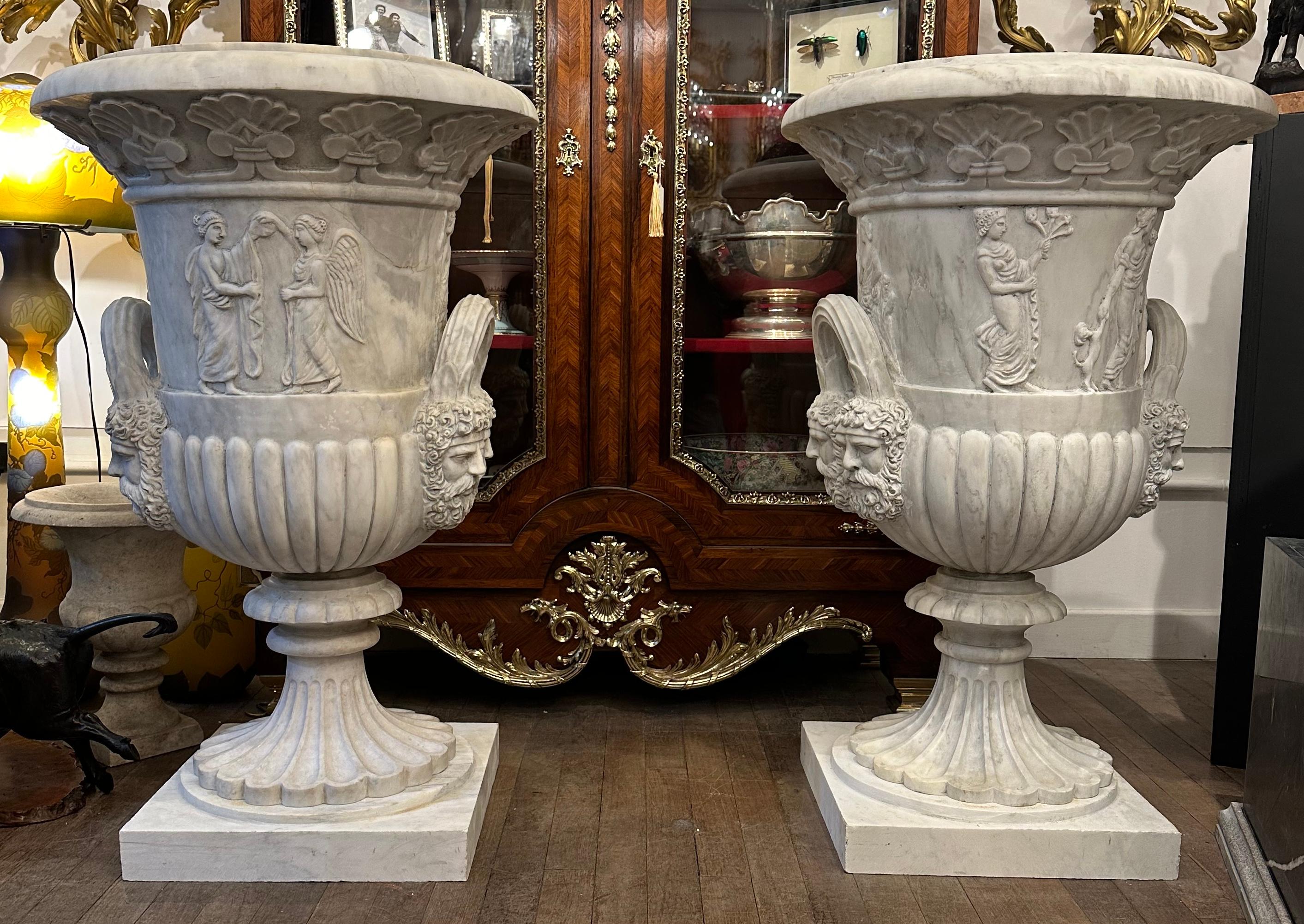 A highly decorative and imposing pair of marble hand-carved urns. Depicting a classical scene including dogs and winged figures which make up the middle section of the urn, with exquisitely carved and bearded heads beneath. The top section has