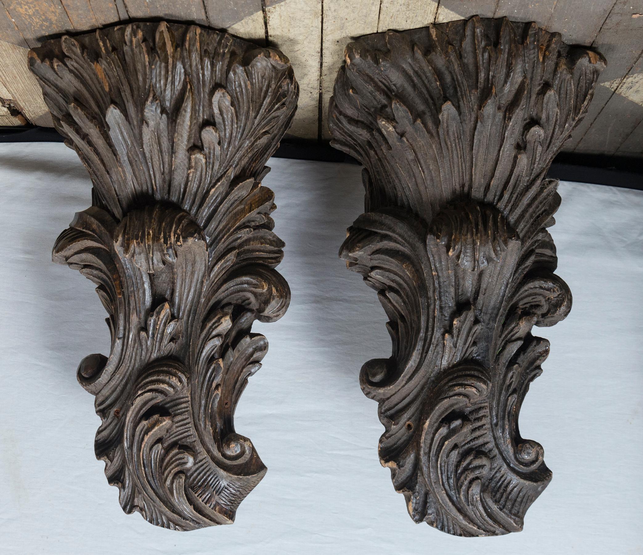 This large pair of hand carved wood brackets have great detailed scrolls and leaves. One appears to be made of one piece while the other is made of separate pieces of wood, glued together to make the whole much like butcherblock is fashioned. In the