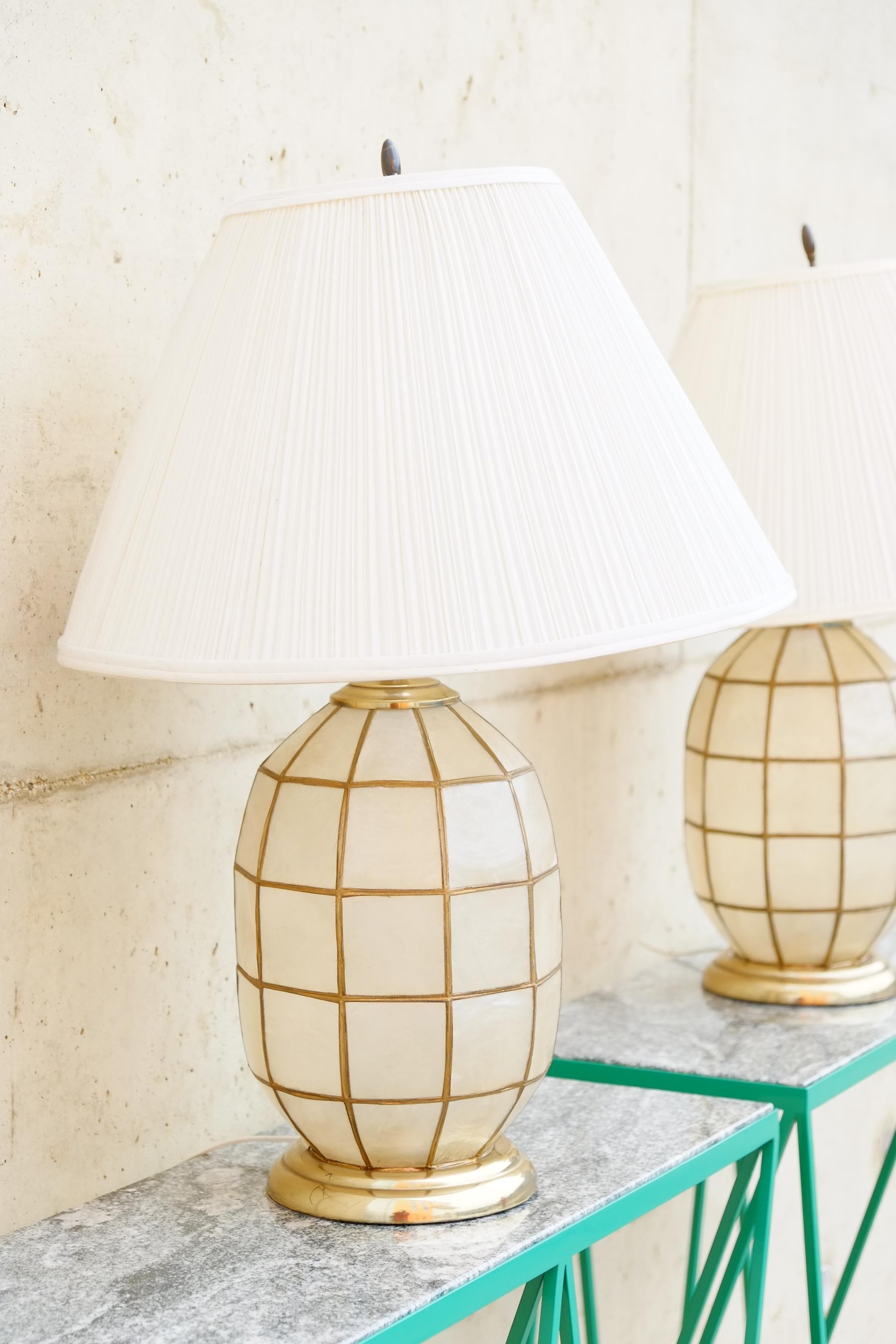 A beautiful pair of large lapis shell table lamps in a Hollywood Regency design from the 1970's. The lamps have a wonderful bulbous lapis shell base with brass soldering around the shells and brass details. Large original pleated lamp shades are