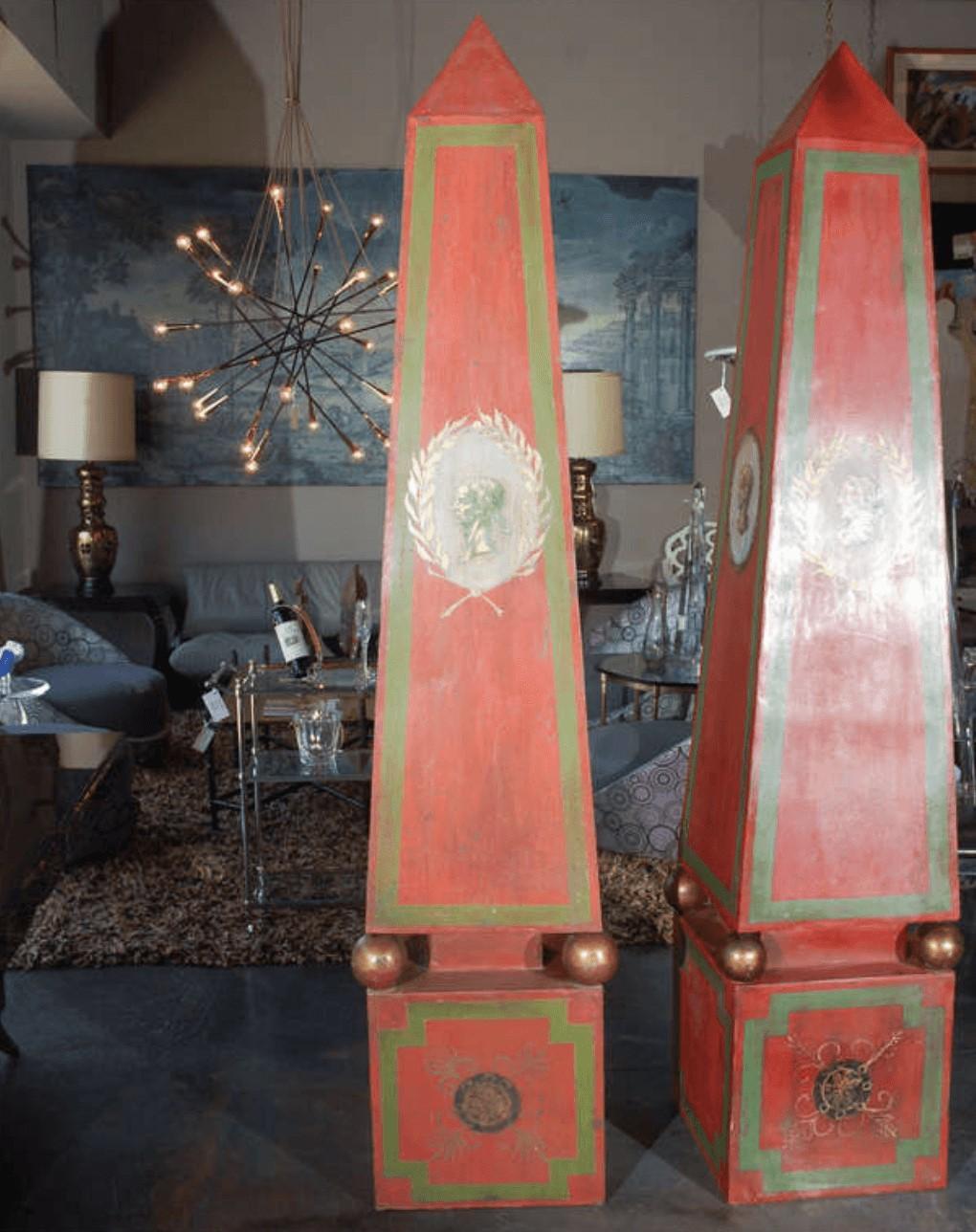 A large pair of vintage Italian tole obelisks in red, green and gold. Sides are decorated with a Roman head (each one different framed by laurel leaves). Front bases are painted with embelished crossed bars with an emblem. Gilded spheres on each