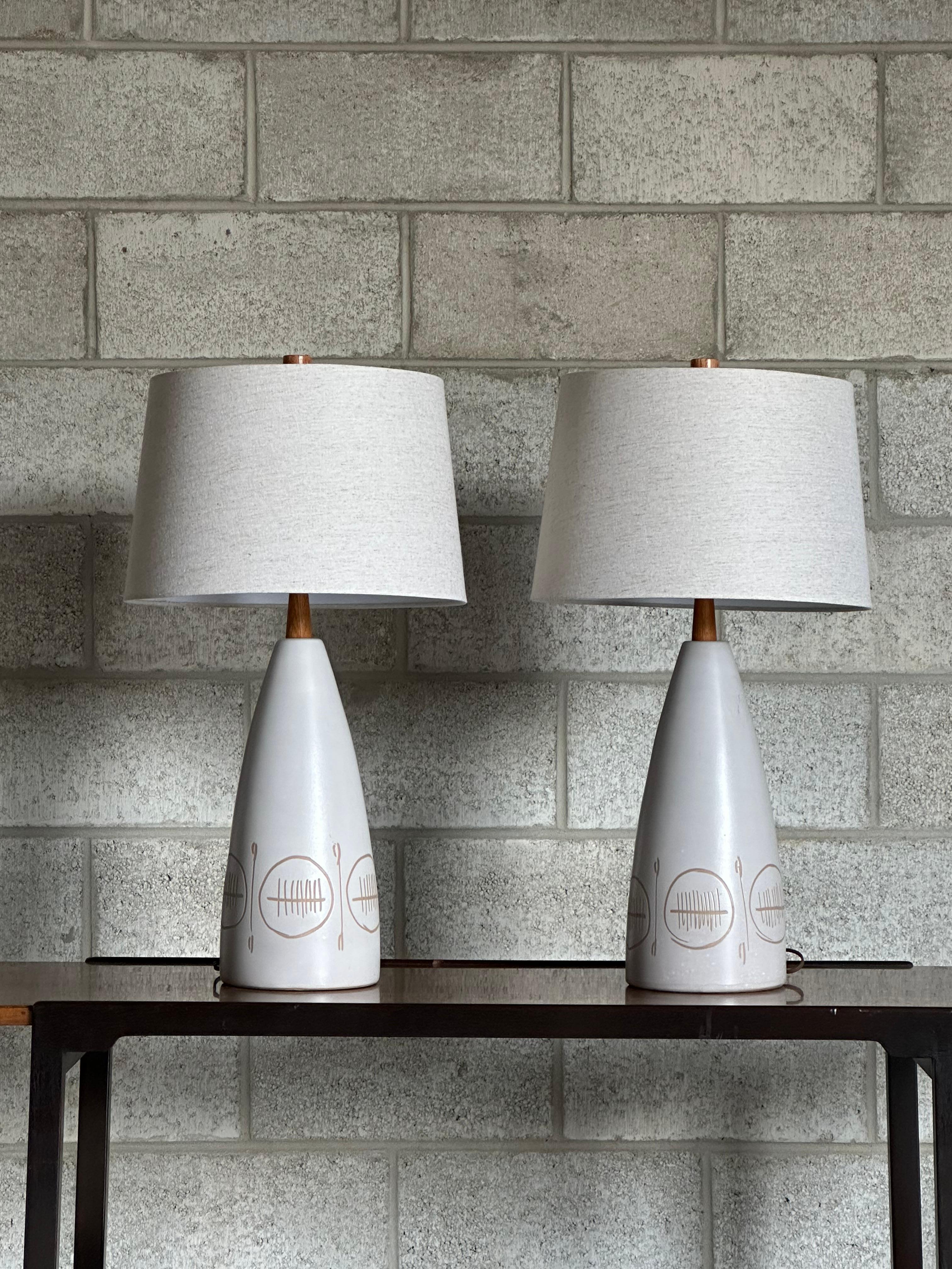 Pair of large table lamps designed by famed ceramicist duo Jane and Gordon Martz for Marshall Studios. Lamps feature a conical body with incised motif. Lamps are completed with oak necks and finials. Lamps present mostly off white with some faint