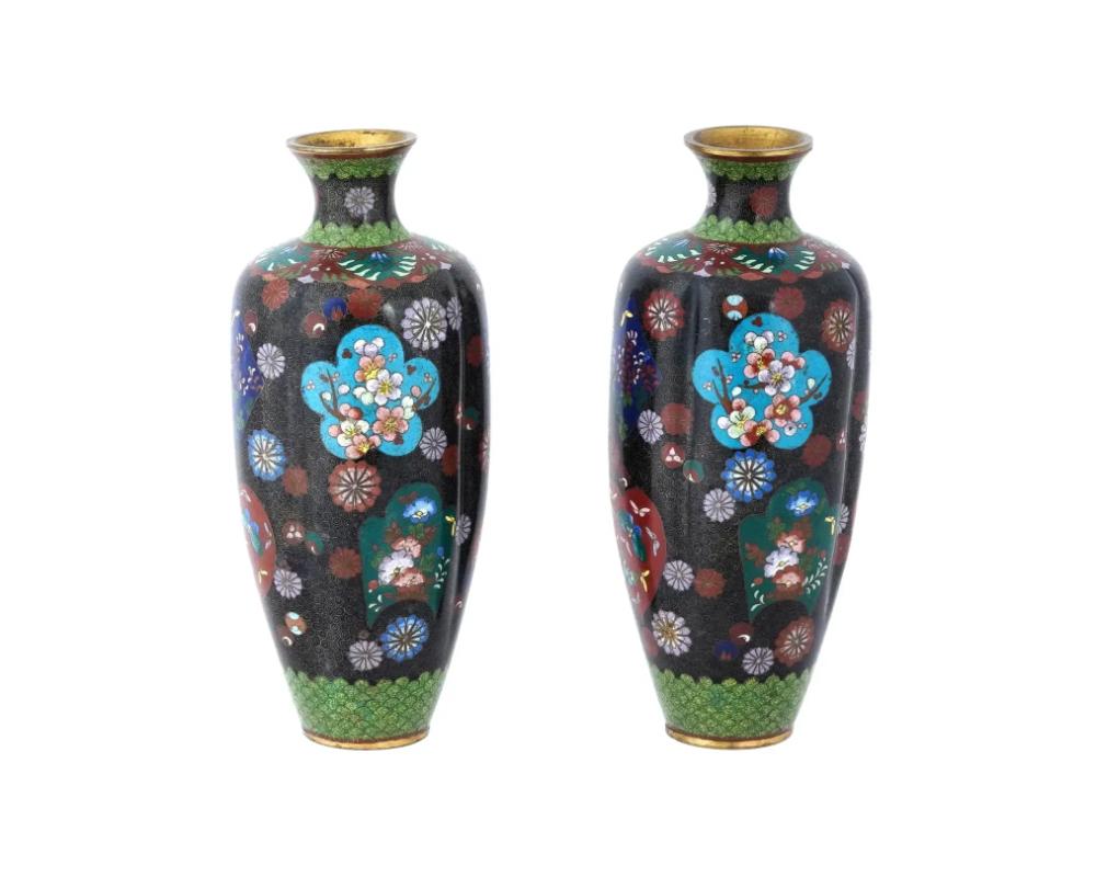 A pair of identical antique Japanese, late Meiji era, enamel over copper vases. Each vase has an urn shaped body and a fluted neck. The ware is enameled with polychrome figural medallions depicting flowers and butterflies in blossoming flowers