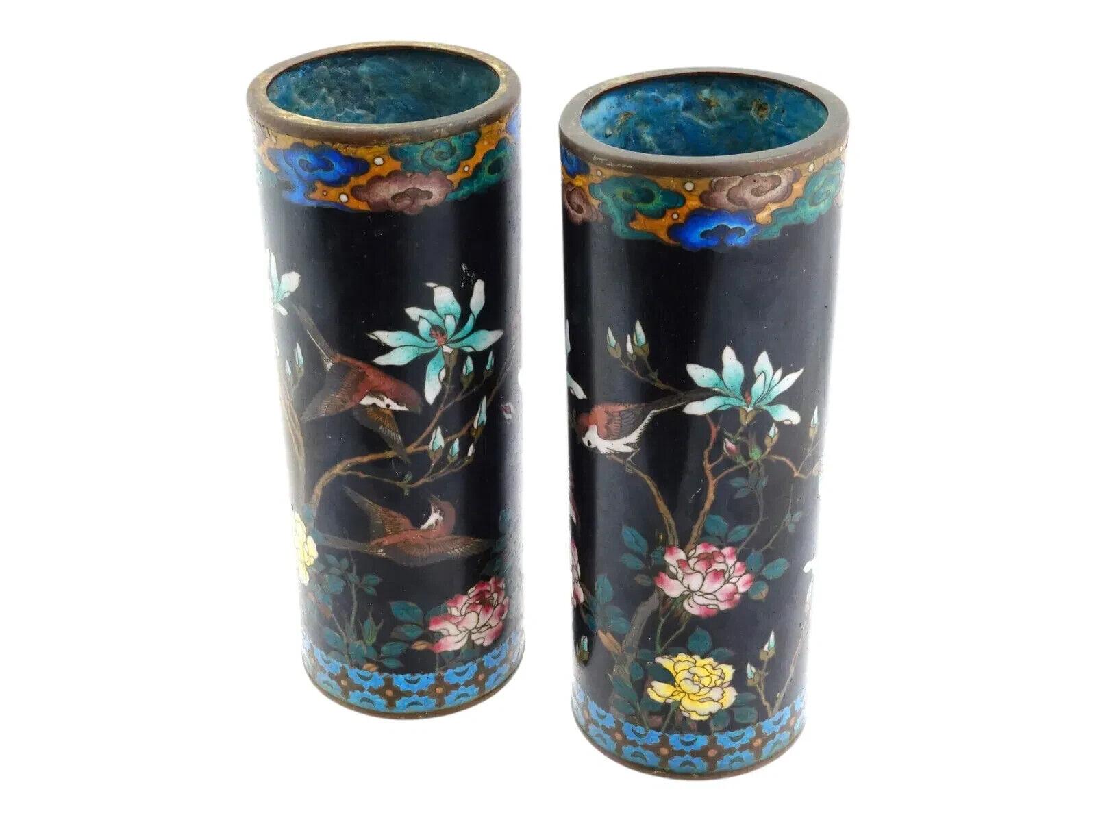 Un par de jarrones japoneses de esmalte sobre cobre. Cada jarrón tiene un cuerpo de forma cilíndrica. Cada jarrón está esmaltado con un diseño policromado que representa pájaros en flores florecientes, realizado con la técnica cloisonné. El cuello y