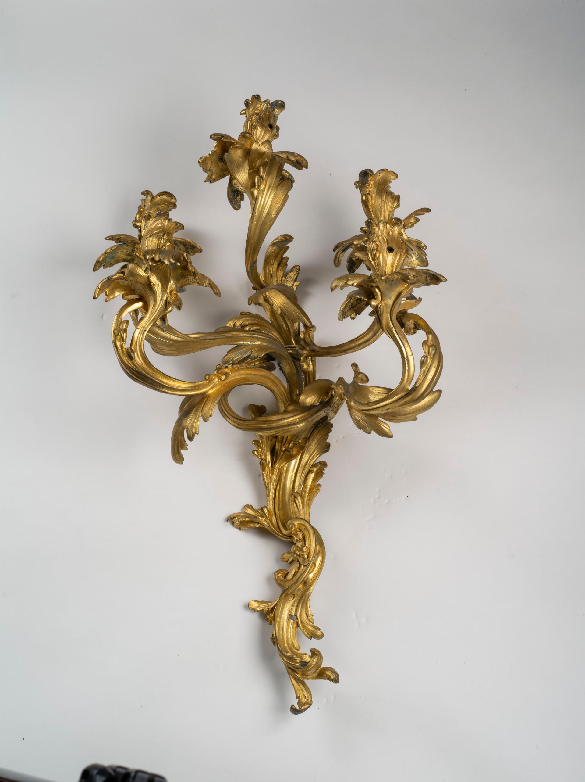 Each sconce of asymmetrical rocaille design with foliate-cast backplate issuing five foliate S and C- scrolling candle arms mounted throughout with stylized leaf-tip motifs. Drilled for electricity.
These magnificent wall lights (or scones) achieve