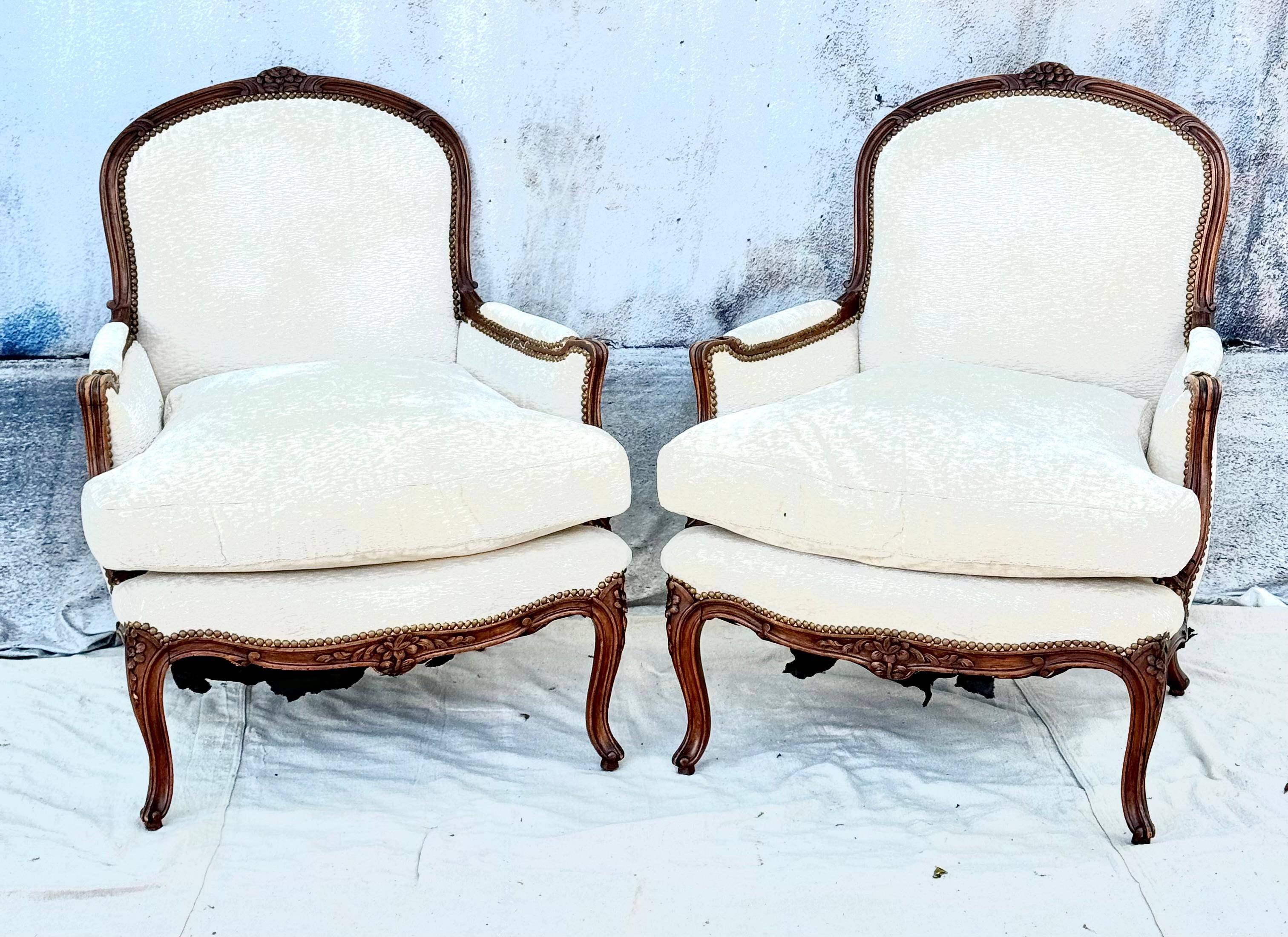 Fabulous large and very comfortable pair of Louis XV Style Carved Beechwood Bergere Chairs. 
The arched molded and upholstered backs with a floral bud continuing to molded arms with padded sides, centering a loose-cushion seat, above a molded seat