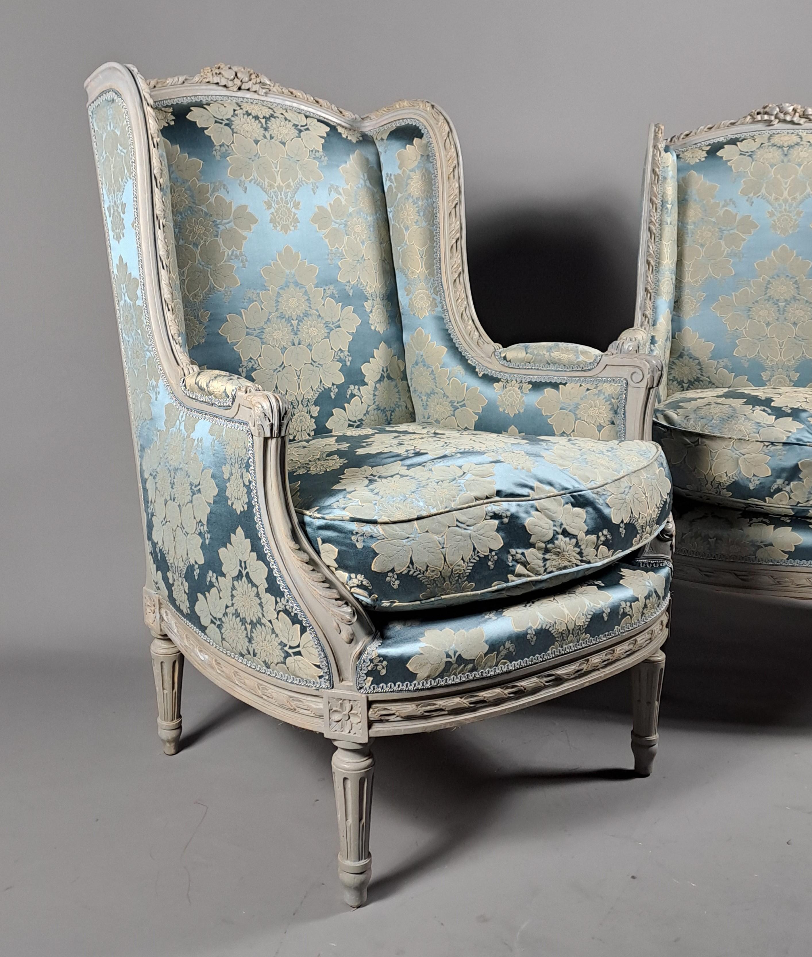 Magnificent pair of large Louis XVI style wingback armchairs in richly carved and gray lacquered wood, covered in a blue/gray satin damask.   

Parisian work  of quality

CIRCA 1880.   

Rich and generous carvings.   

Completely reupholstered by