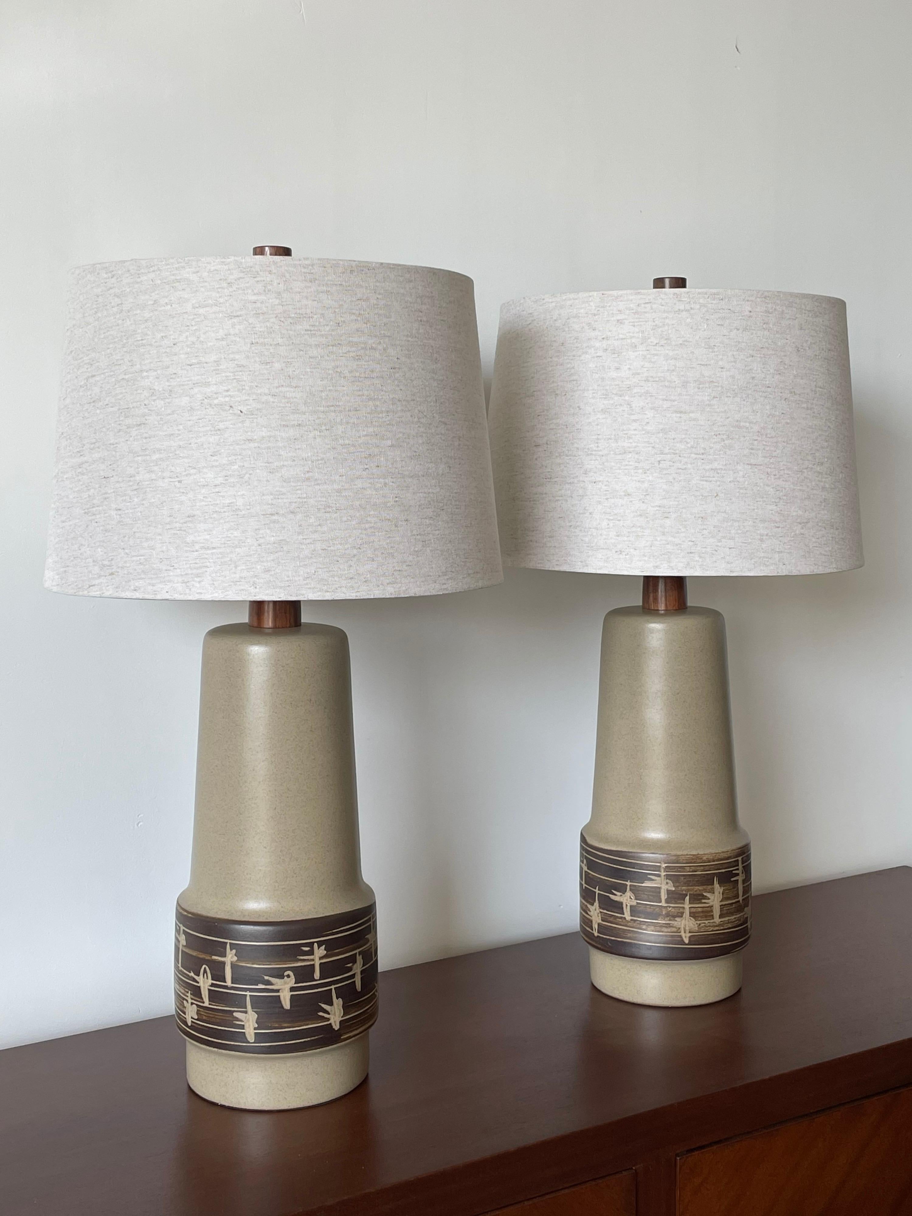 Large pair of lamps by ceramicist duo Jane and Gordon Martz for Marshall Studios. Wonderful tan color with faint blue speckles with patterned detail around bulge. 

These lamps were sourced as “new old stock” ceramic lamp bases. They are authentic