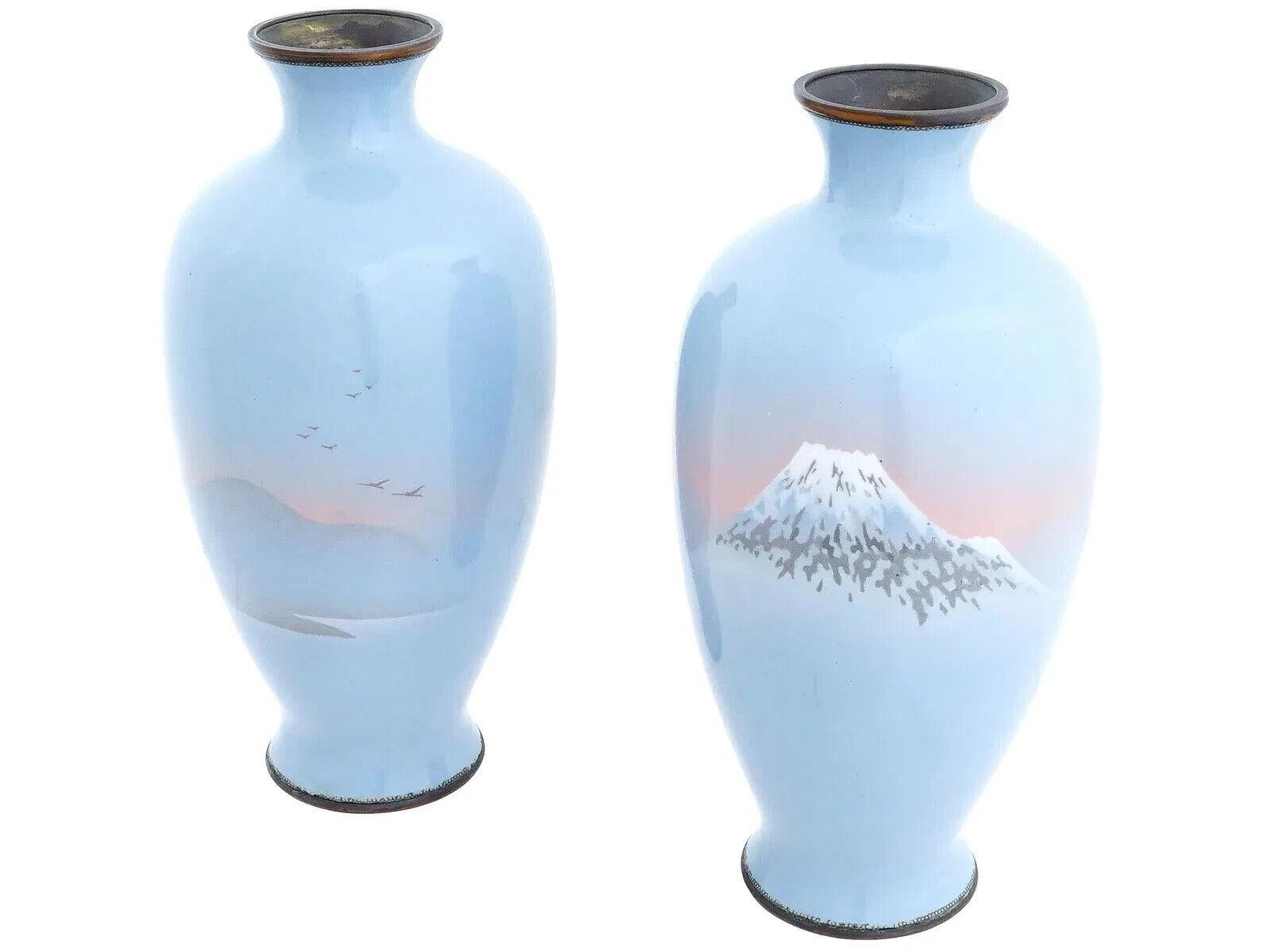 A pair of antique Japanese Meiji Era wireless cloisonne or musen shippo vases. The vases have a light blue ground with a landscape depicting Mount Fuji on one vase and a landscape with distant mountains and flying birds on the other. Both vases have