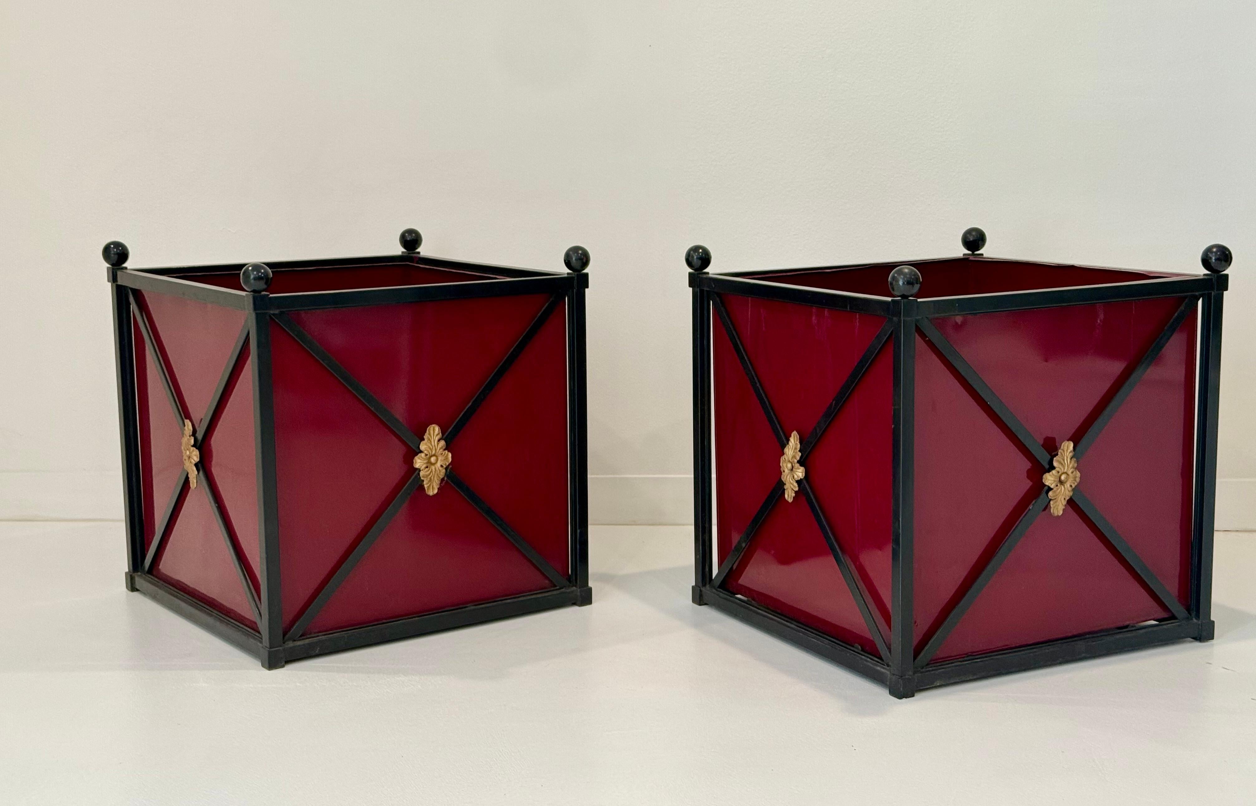 A bold and architectural pair of Neoclassical-style metal planters, each measuring an impressive 33 inches square. These striking vessels feature deep burgundy lacquered panels framed in matte black metal with crisply executed X-form crossbars. At