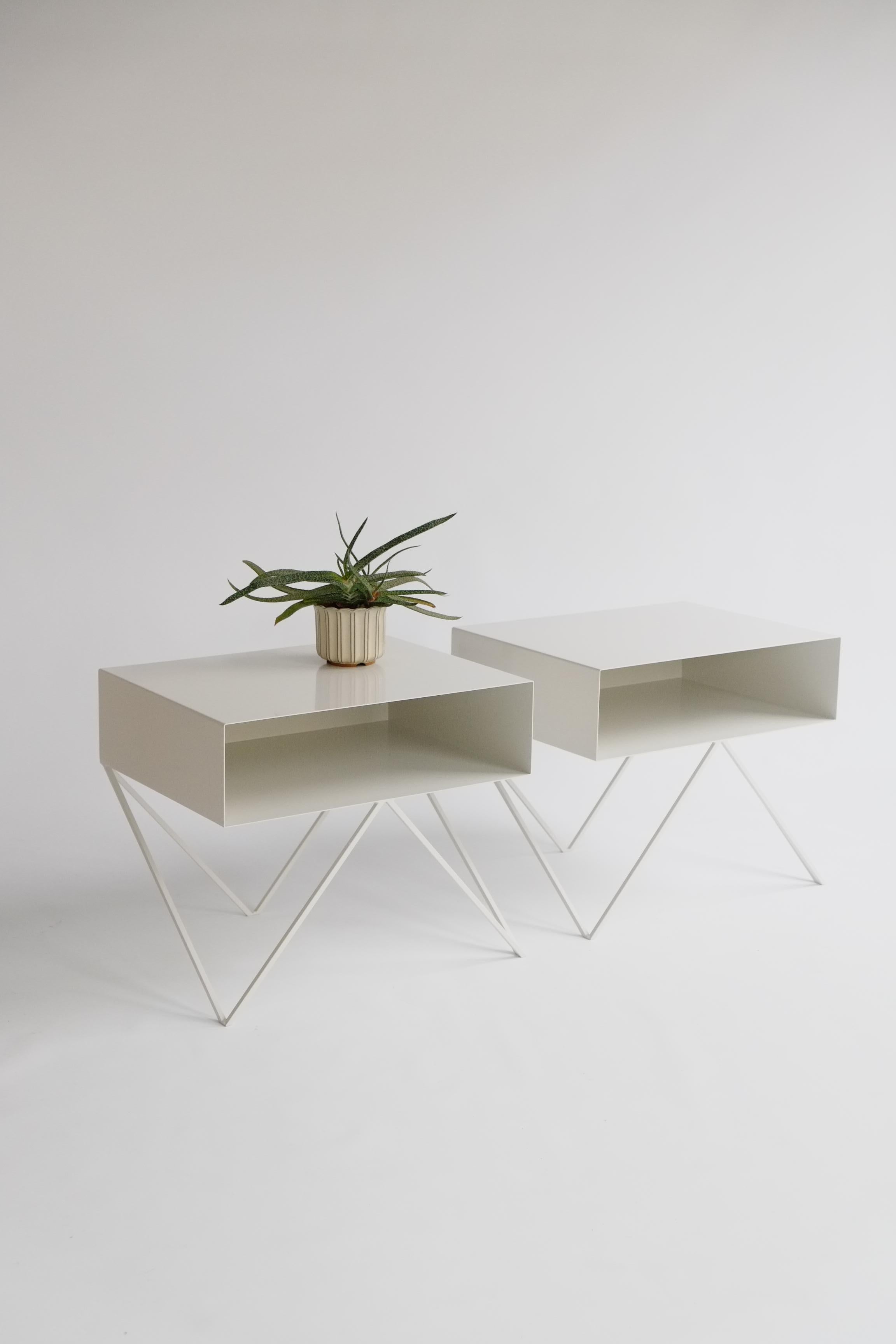 A bespoke pair (size customisable) of elegant paper white powder-coated steel Robot bedside tables. The Robot side table features an open shelf on zig zag legs. A wide, low elegant design made of solid steel, powder coated in paper white. The clean