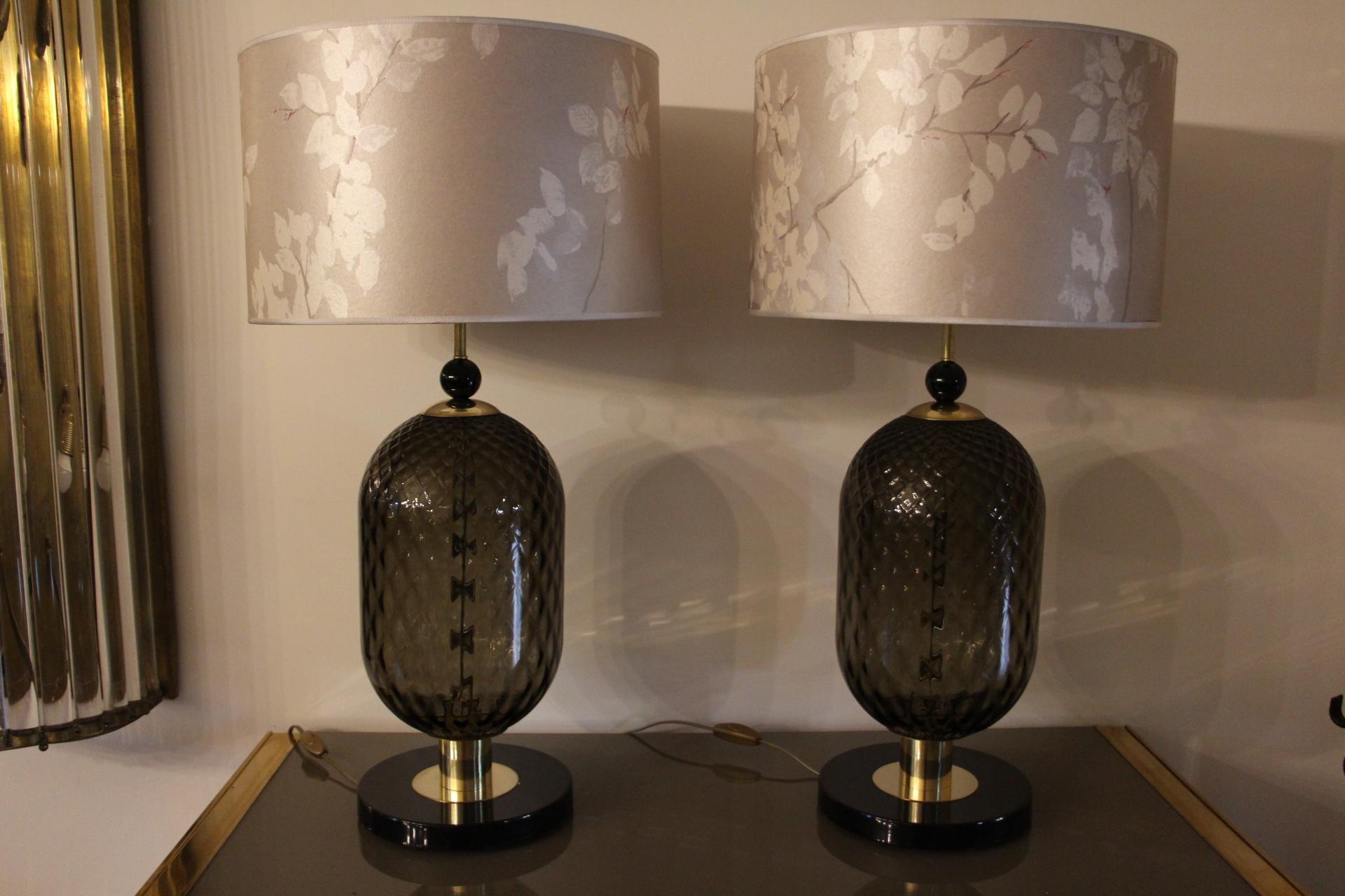 This impressive pair of table lamps is made in a very nice smoke color honeycomb glass. Their volume is really unusual, they are 22 cm large.
Its base is made of a deep piece of black Murano glass that reminds its top black glass ball.Its main body