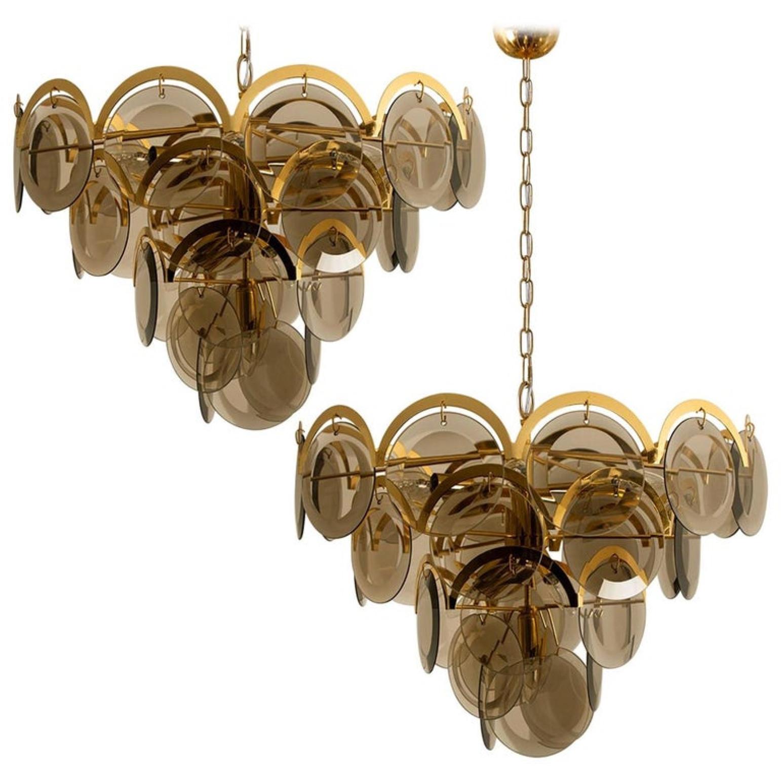 A gorgeous four tiers hanging light fixture, attributed to Vistosi with graduated tiers of 33 smoked round facet chapped glass discs framed by half-moon shaped brass. The chandelier is complete, no hook or glass disk is missing, with its original