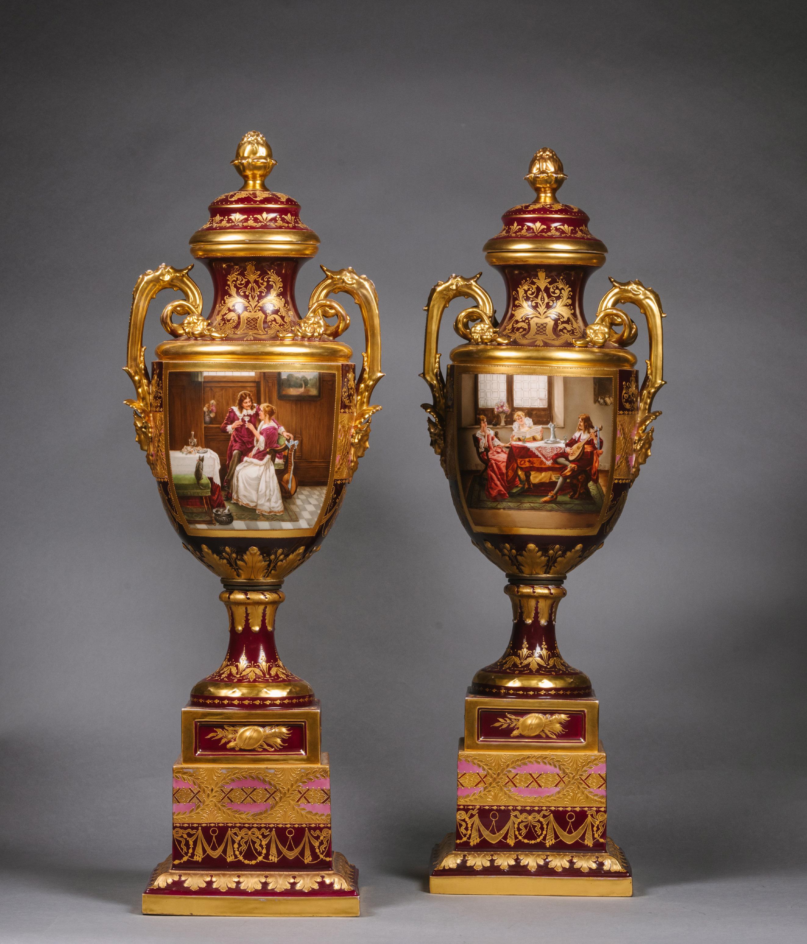 A Large Pair of Vienna Style Porcelain Ruby Ground Vases, Covers and Stands.

Blue Beehive marks and each twice signed 'Wagner'.

Each cover with pine cone finial. The baluster shaped vases with loop handles with  foliate and maiden mask terminals.