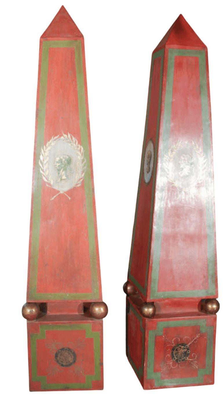Une paire rare et frappante de grands obélisques italiens en tole, peints à la main dans de riches tons de rouge, de vert et d'or. Chaque face présente un motif unique de tête romaine encadrée de feuilles de laurier, offrant une élégance classique