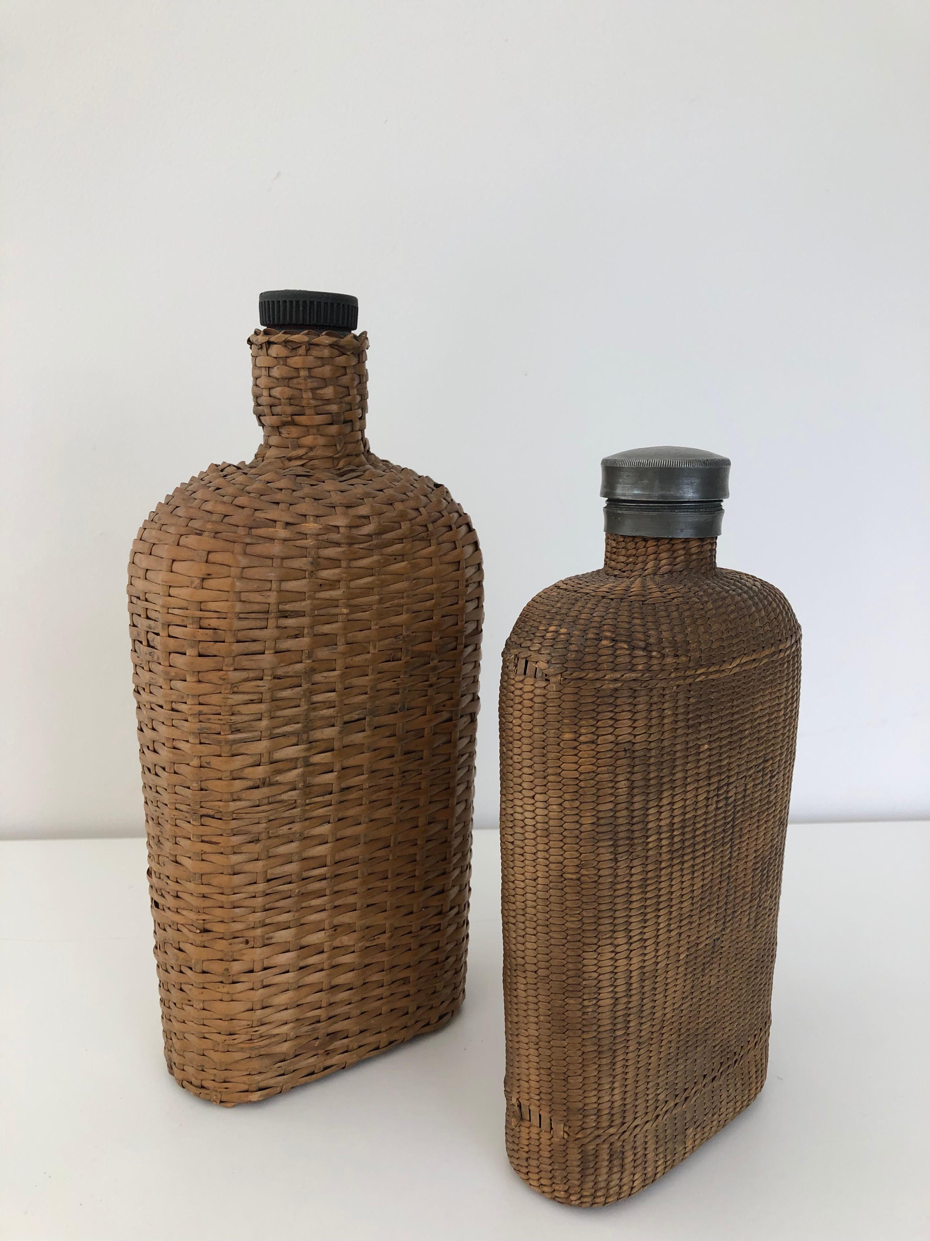 A large pair of vintage wicker over glass flasks. One with pewter stopper. Largest measures 10