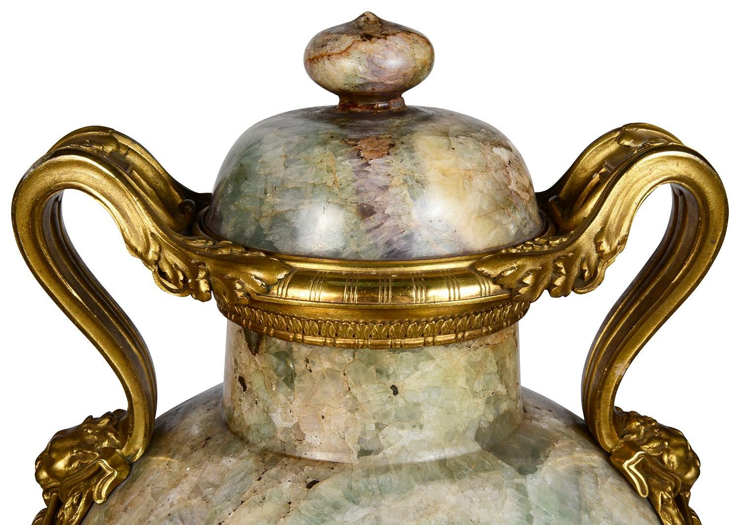 A spectacular pair of early 19th Century French Florite Beige lidded marble urns, each with wonderful mercury gilded ormolu mounts and handles with scrolling foliate and petal decoration, Lion mask and ring-drops to either side. Raised on circular