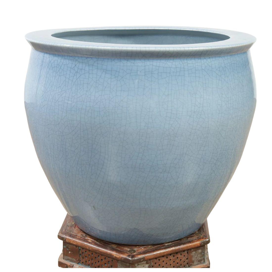 Eine große hellblaue Jardinere mit runder Öffnung oben, die auf einem Holzsockel mit detaillierten Schnitzereien mit indonesischen Motiven ruht. Das glasierte Porzellan verleiht der Schale ein schönes Craquelé-Finish.  Groß genug für einen Baum oder