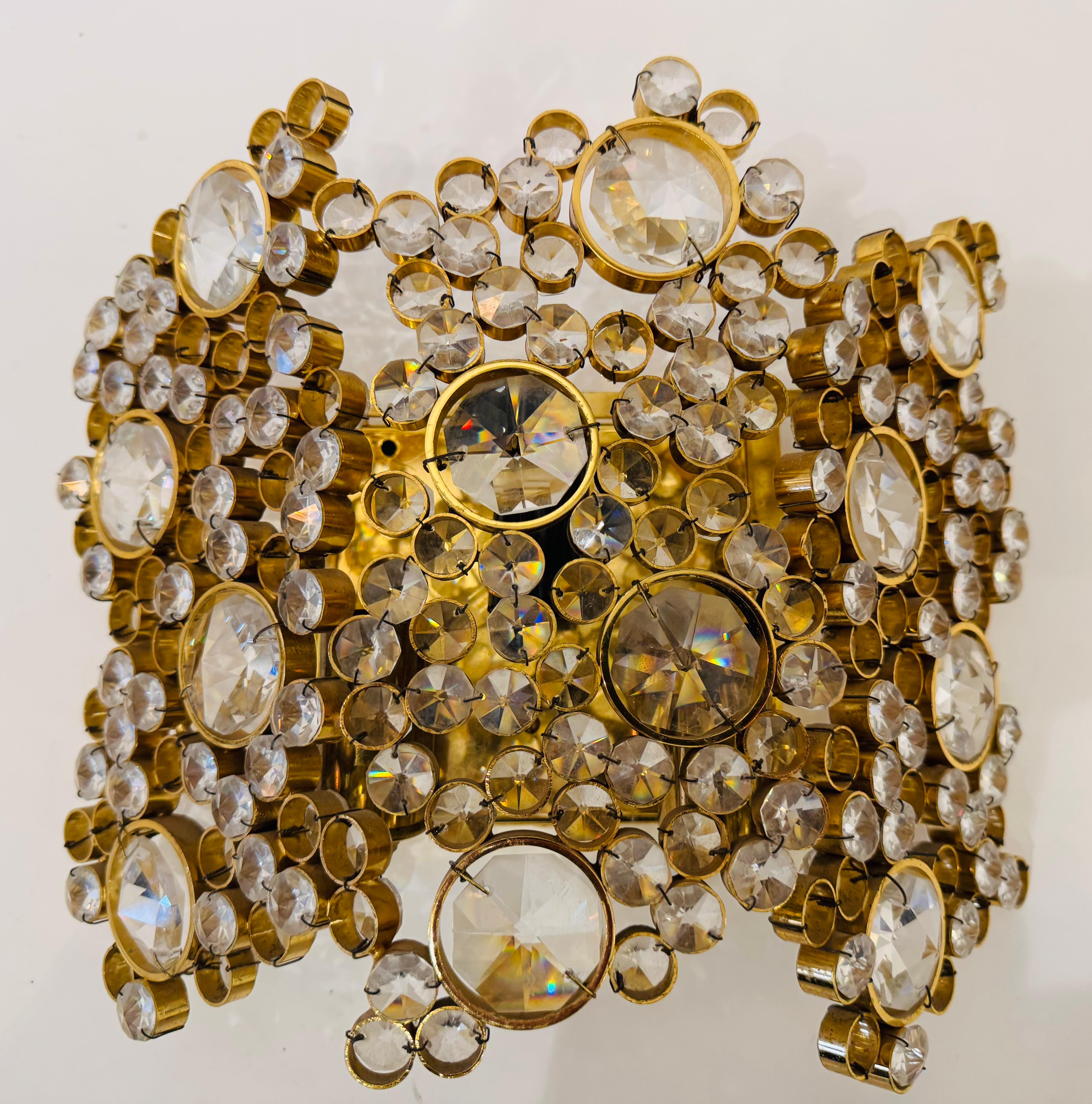 Precioso y lujoso aplique de cristal austriaco de mediados de siglo de los años 60, compuesto por numerosos cristales tallados engastados en un marco chapado en oro, obra del fabricante de iluminación , Palwa. Recableado. 3 tomas de candelabro.