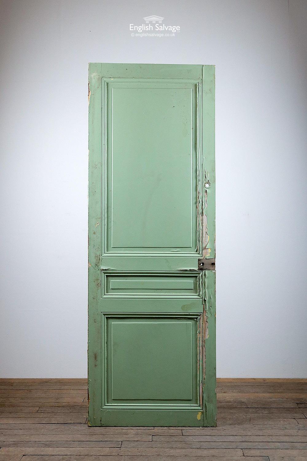 Tall reclaimed pine panelled door from France. Three raised and fielded panels both sides. Painted green one side and white to the other, flaking in places. Old fitting holes.