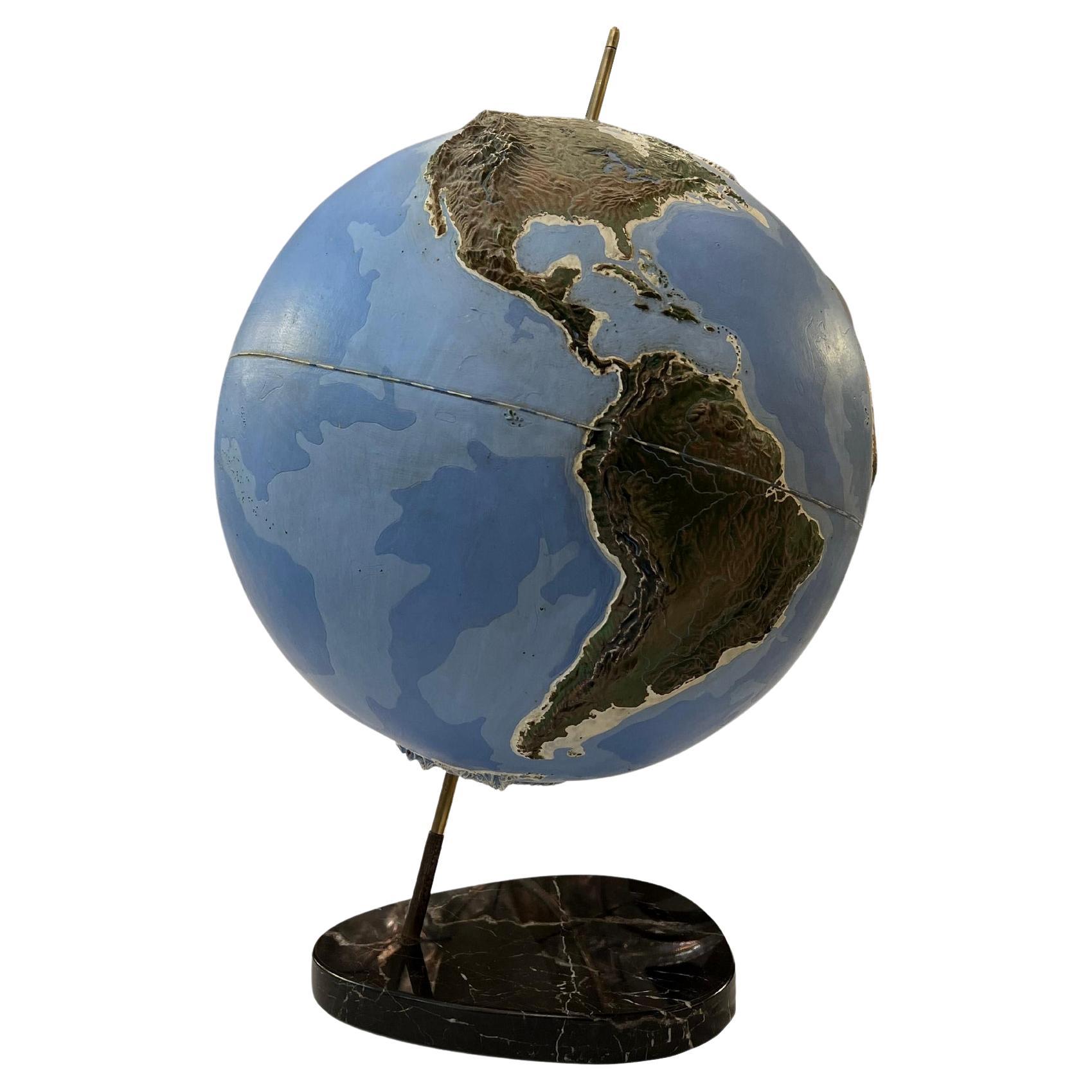 Important globe terrestre en relief représentant les océans et les continents.
Le globe est en plexiglas peint, fixé à la base en marbre par un axe en laiton. France vers 1950.