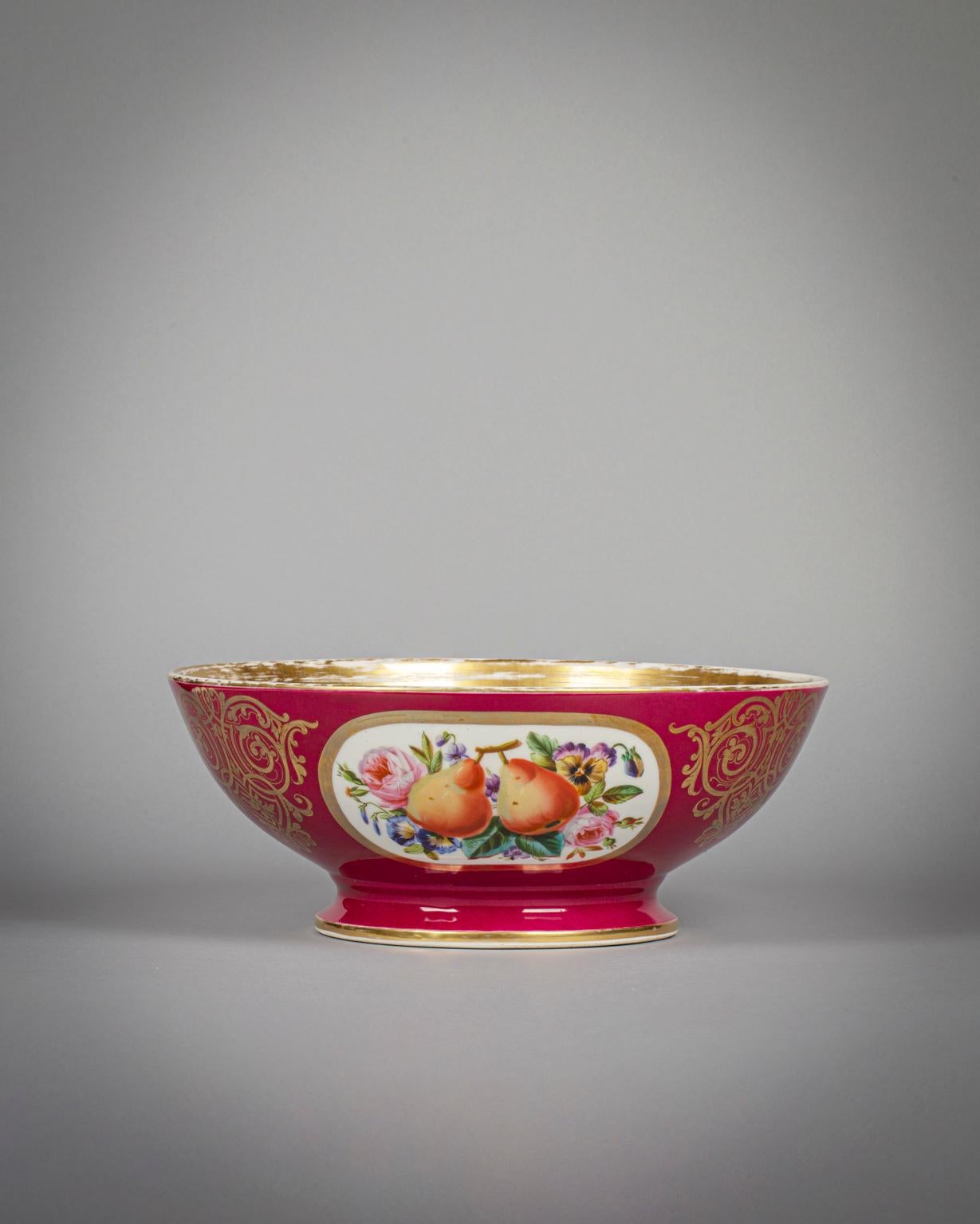 With three gilt border oval panels painted with fruit, flowers and foliage with alternating gilt scrollwork all on a ruby ground. 