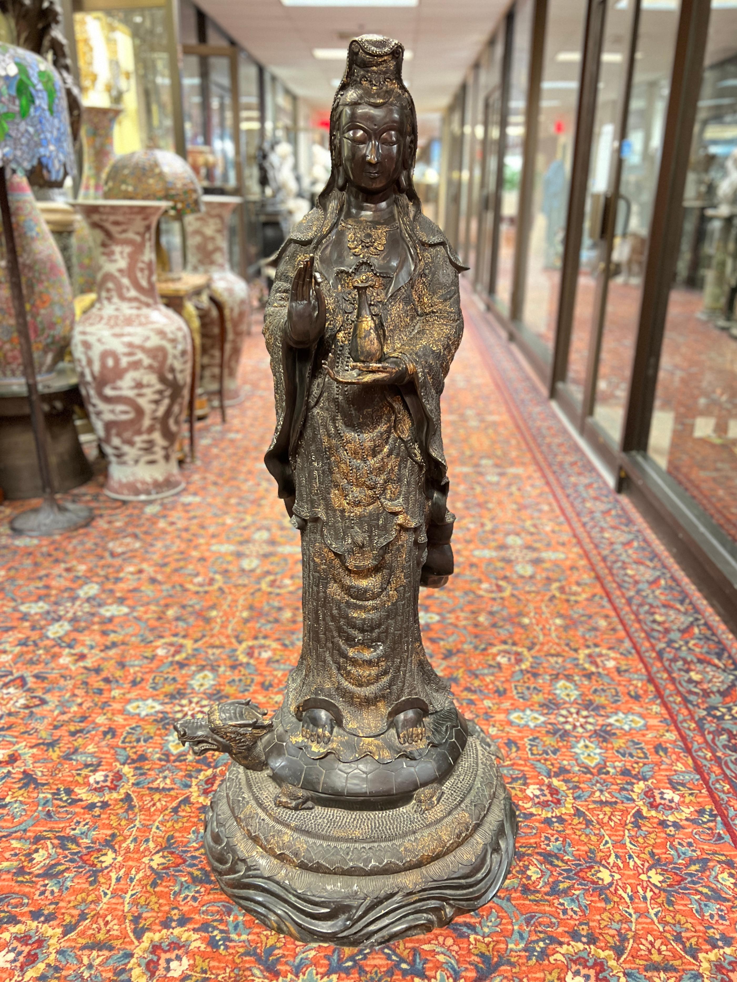 Estatua de Guanyin, de bronce patinado con reflejos dorados, que sostiene una botella de agua purificadora, de pie sobre el lomo de una tortuga, simbolizando su papel de protectora (en particular de los pescadores) y representando la longevidad y la