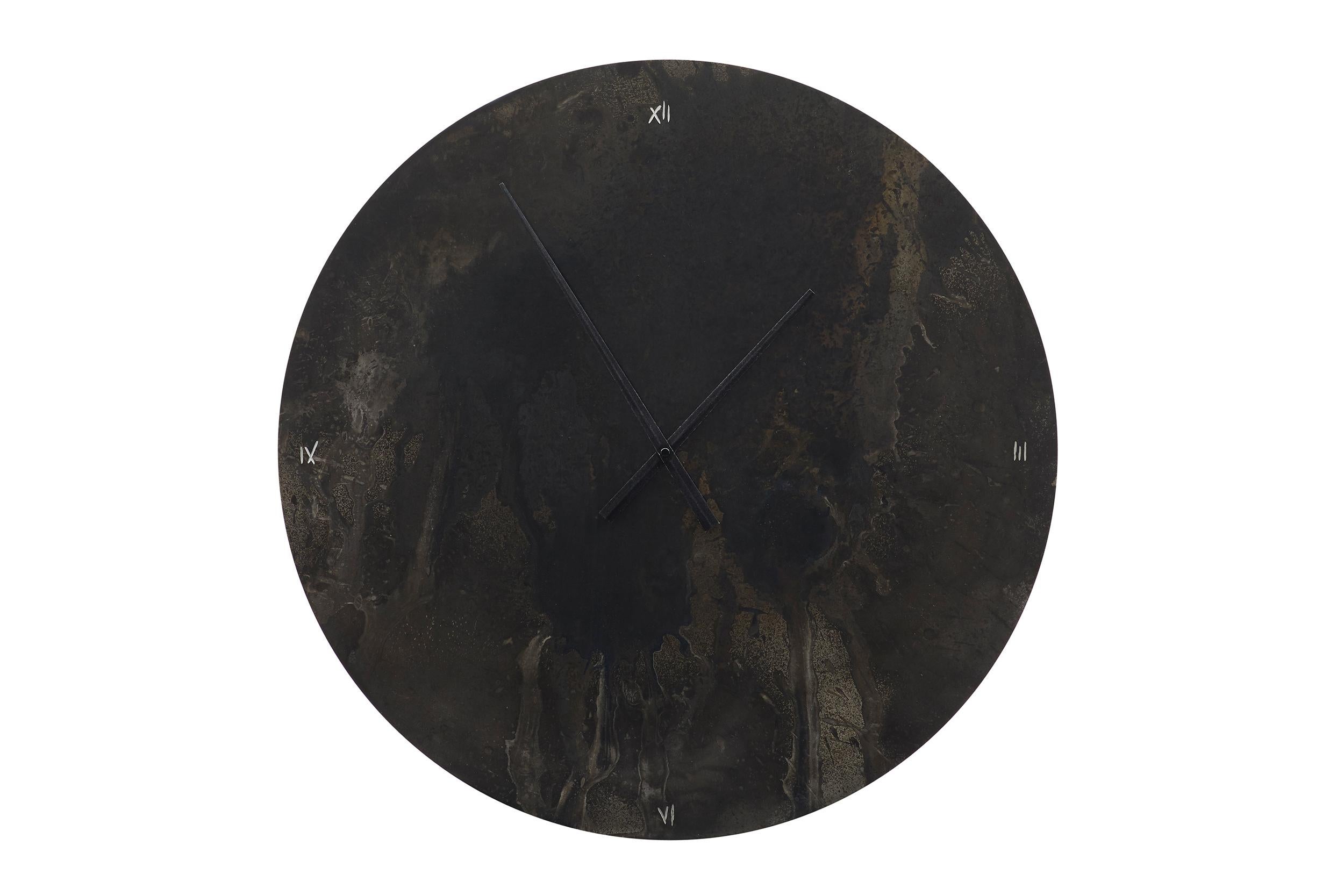 Este impresionante reloj de pared está hecho de acero cortado, calentado por puntos con un soplete y pintado con diferentes óxidos negros para evocar una profundidad cálida y vibrante en un material habitualmente frío. A continuación, el acero de