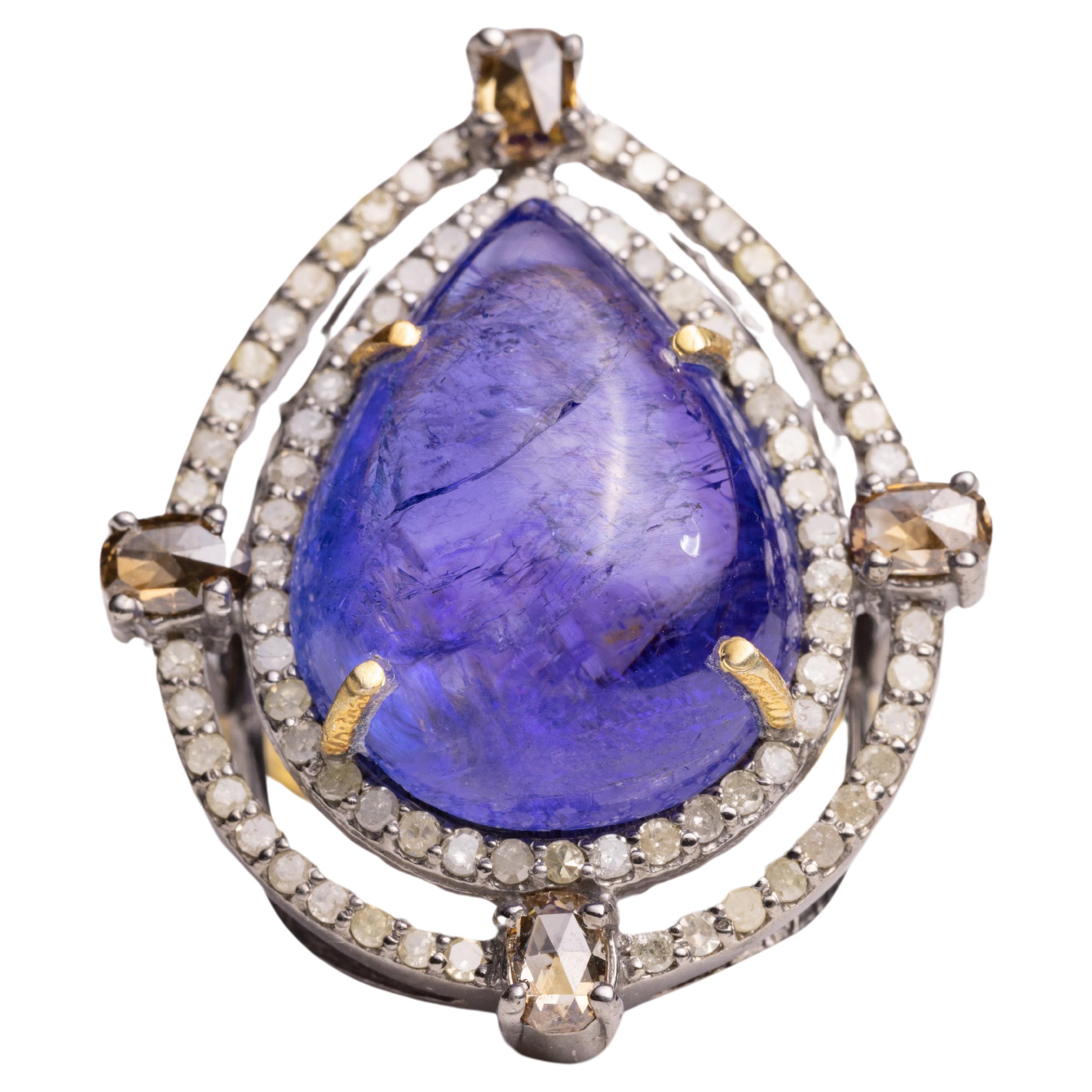 A lovely, large pear-shaped cabochon Tanzanite dome cocktail ring bordered with two rows of round, brilliant cut diamonds and champagne diamonds on the four sides.  Diamonds also along the shoulder of the band.  Set in sterling silver and 18K gold