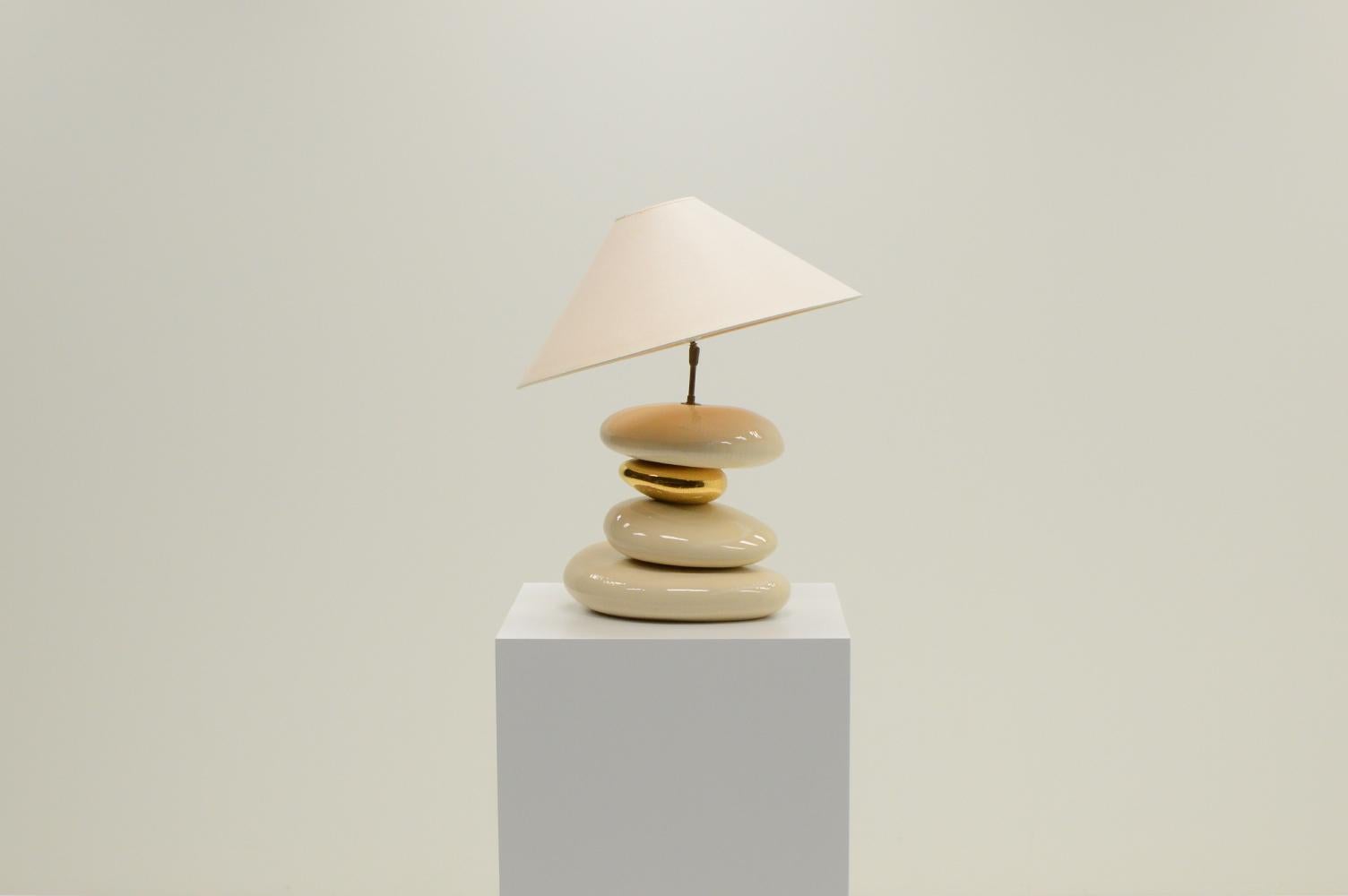 Large Pebble table lamp by François Chatain, 1980s France. Four ceramic pebbles, one gold and 3 off white. The angle of the shade is adjustable thanks to the brass ball joint mechanism. The original fabric shade has a light stain (see picture).