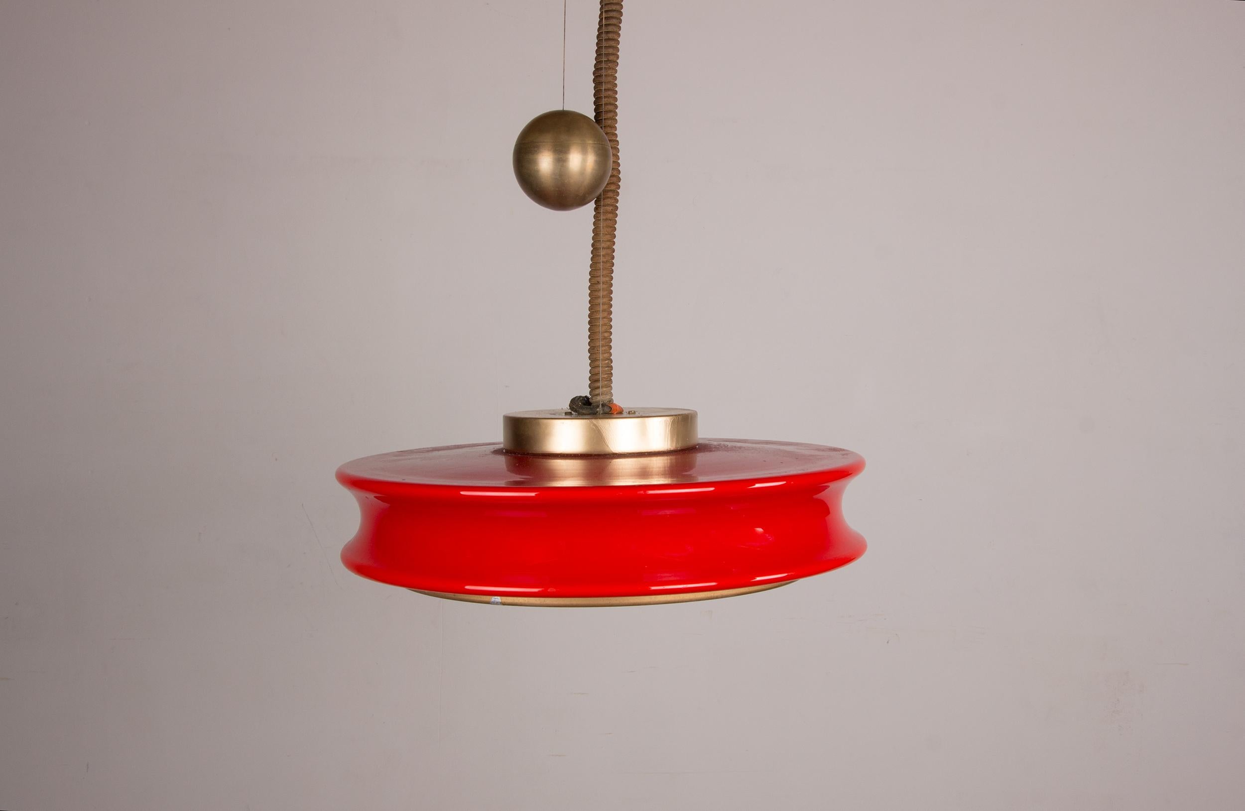 Exceptionnel grand lustre suspendu avec un lourd contrepoids sphérique en laiton pour le réglage de la hauteur, un magnifique diffuseur circulaire et profilé en verre rouge, et une grille dorée avec un motif concentrique à la base.

Il comporte