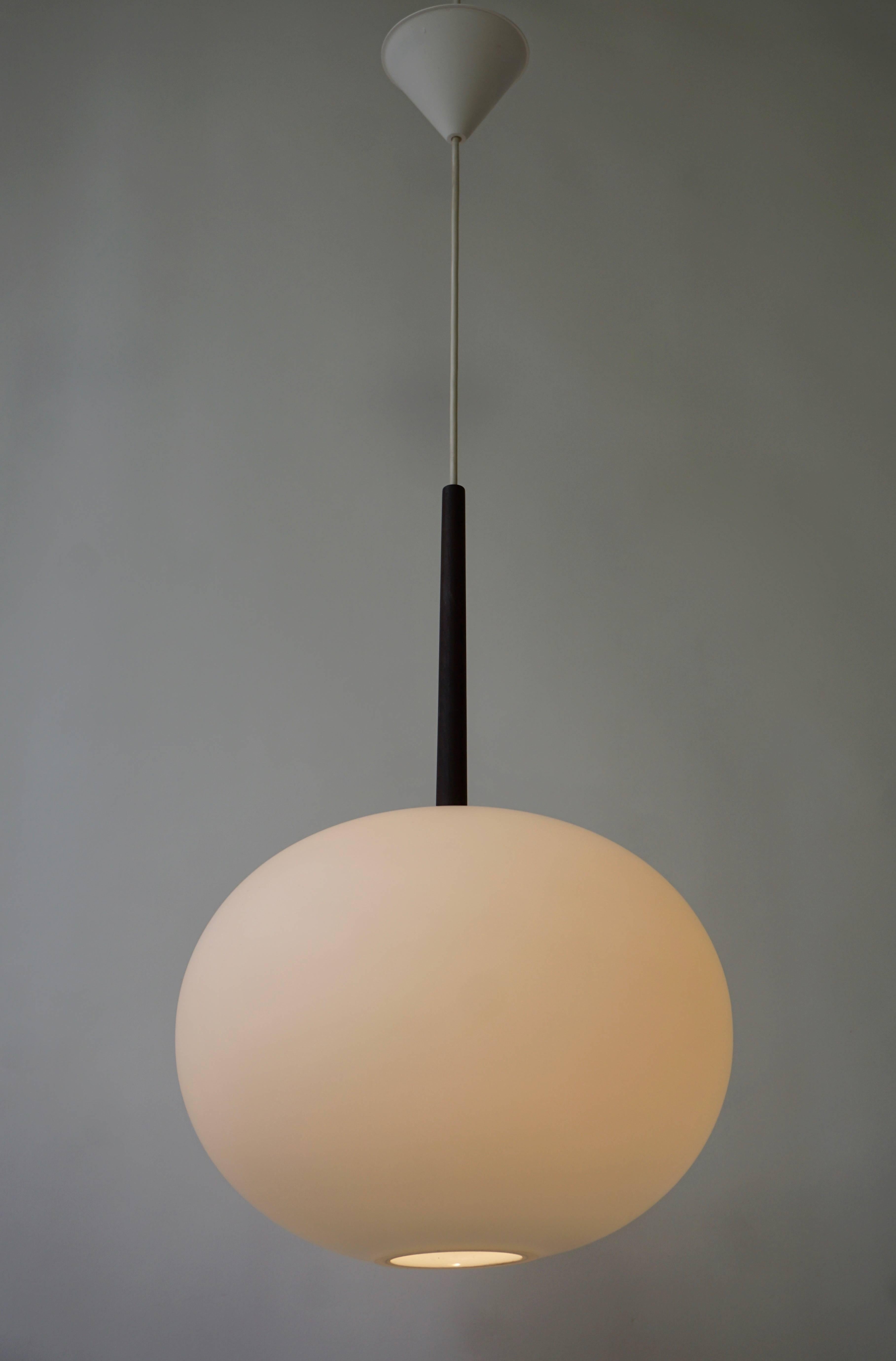 A beautiful pendant in oak and opaline glass by Uno & Östen Kristiansson for Luxus, Sweden. The lamp is suspended by one wire from the canopy and divided by a piece of wood on the shade. The shade is made of opaline glass. The round shade creates a