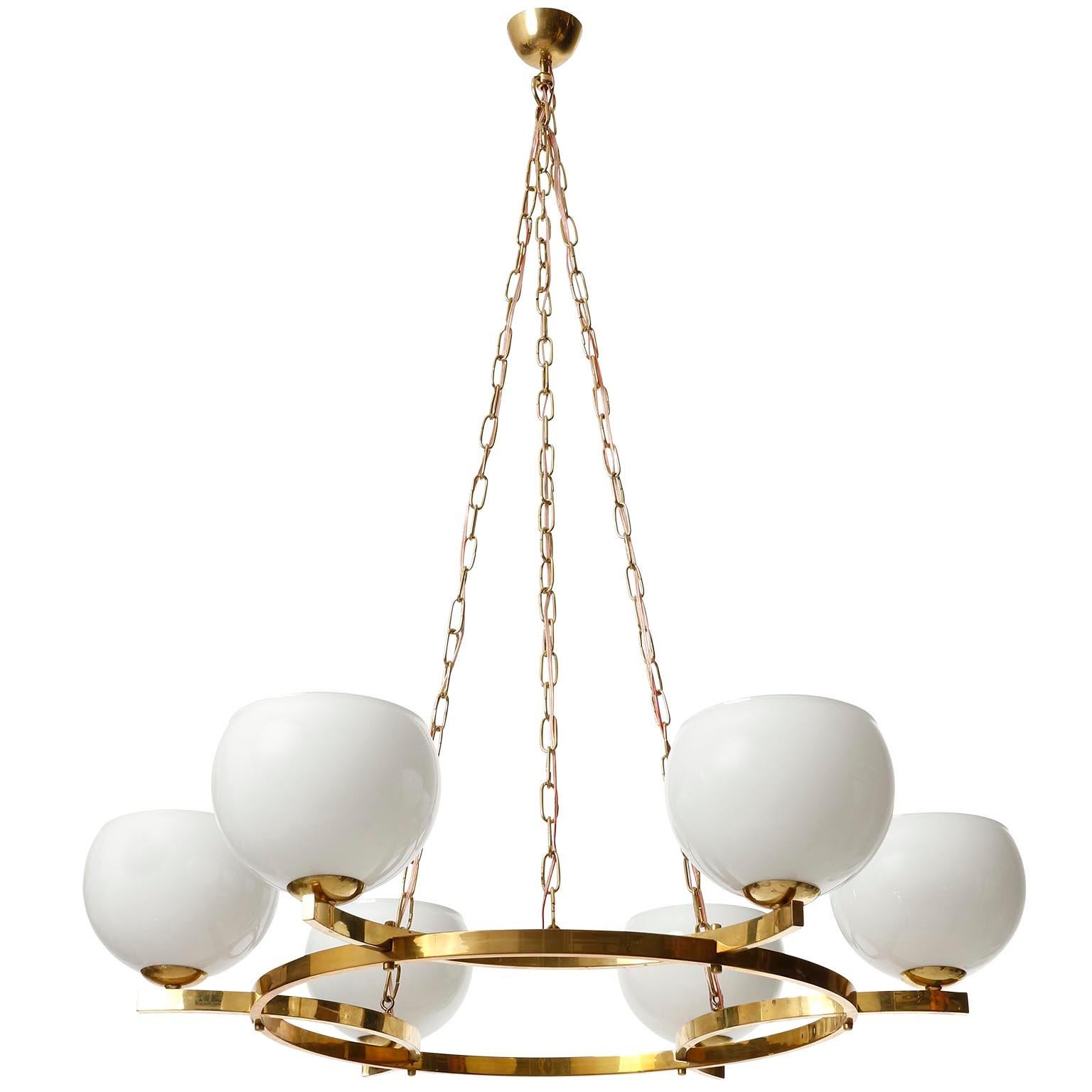 A large pendant chandelier manufactured in midcentury, circa 1960 (late 1950s or early 1960s).
This geometric shaped fixture is made of a polished solid brass ring with little patina and opaline glass lamp shades. The light body is suspended from