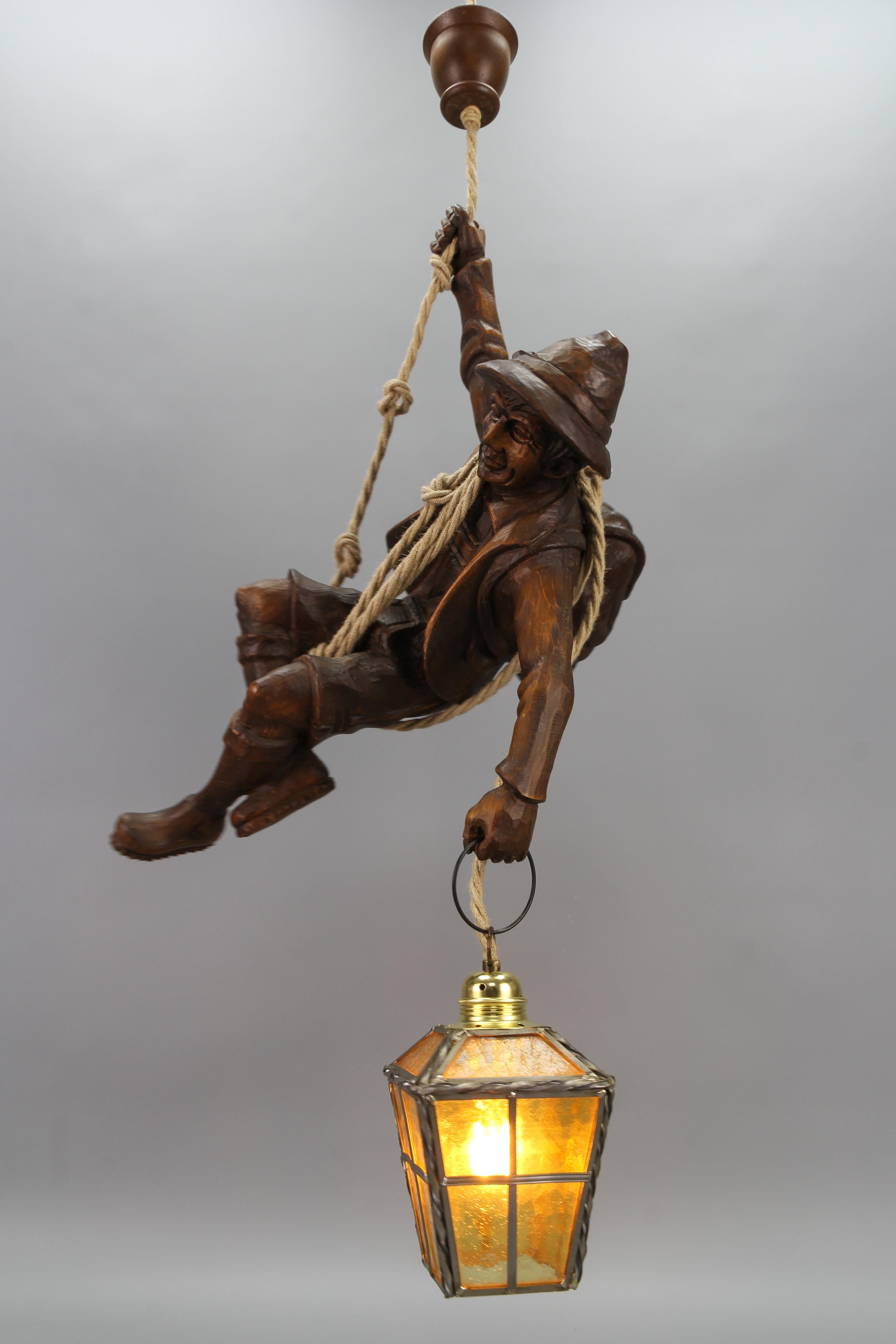 Large Pendant Light Fixture with Carved Climber Figure and Lantern, Germany
This impressive German figural pendant lamp features a masterfully hand-carved linden wood figure of a handsome mountain climber in natural brown wood tones. The detailed
