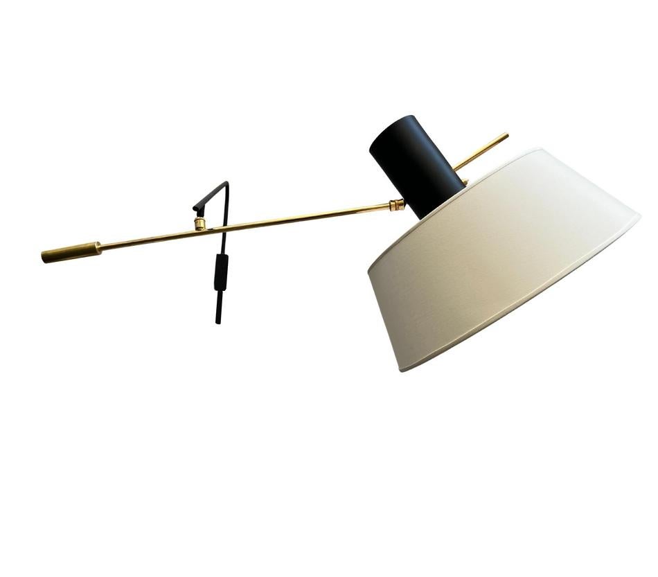 Rare Maison Lunel sconce with inverted shade, designed and produced circa 1960. Composed of a black-lacquered metal arm with wall mounting, terminated by a brass ball joint supporting the second arm fitted at one end with a brass counterweight, and