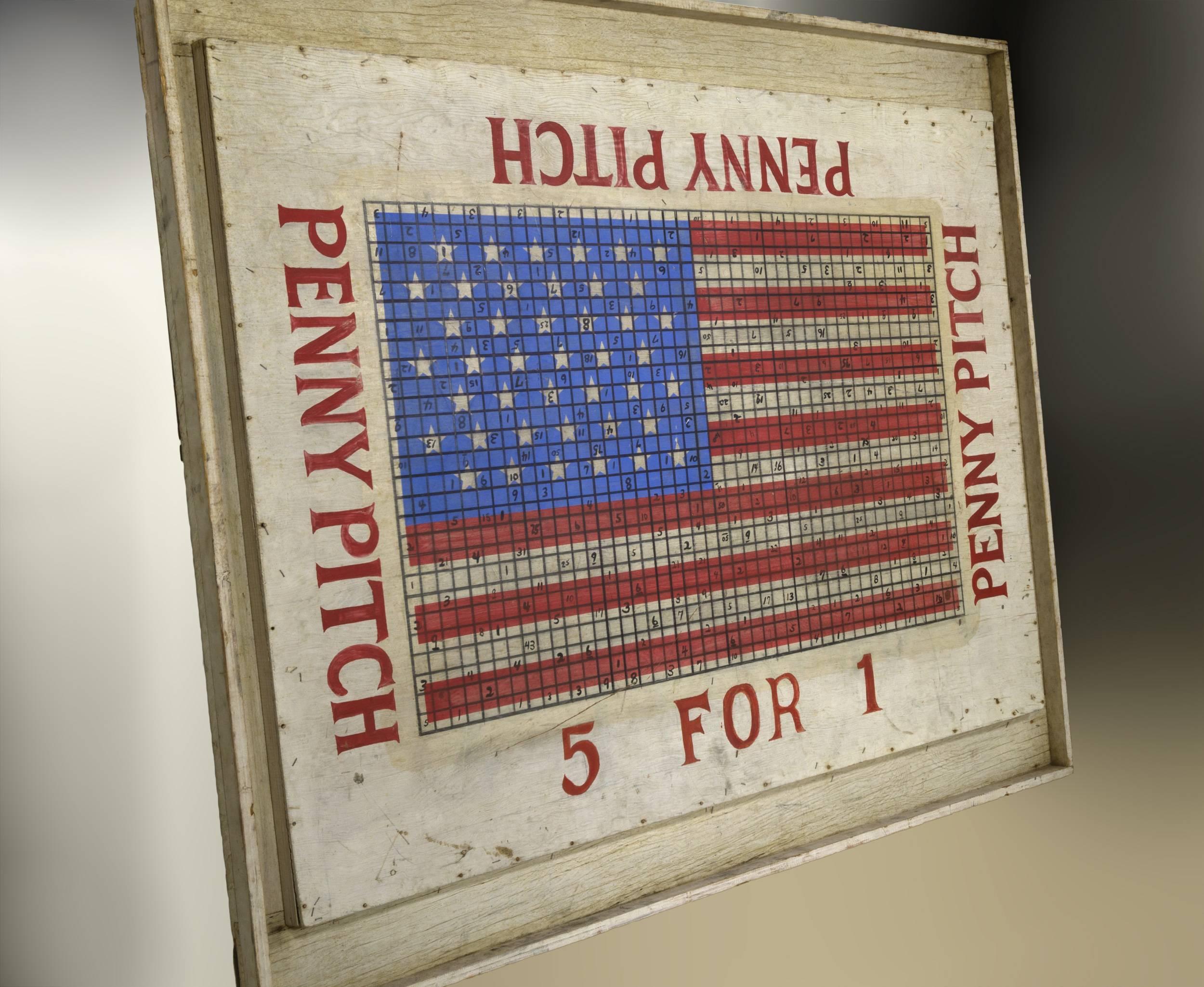 Graphic American flag that’s painted over
plywood with a molded edge and surrounding ditches on all four sides
to catch the sliding pennies. It originally had legs it is now a
piece of vernacular art now hangs on a wall like a