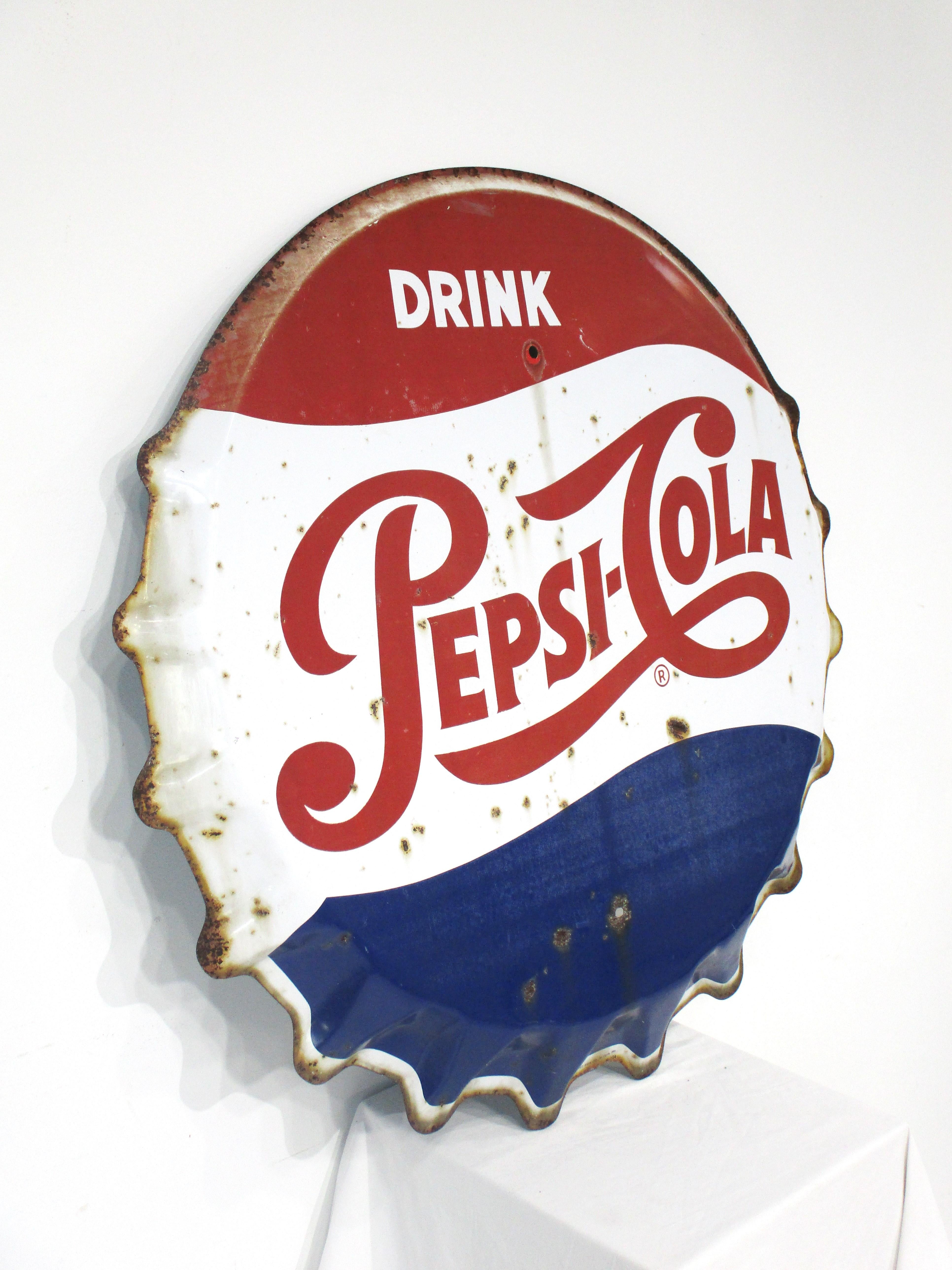 A large sized vintage metal formed pressed bottle cap sign painted in the red, white and blue colors of the Pepsi Cola soft drink company . Found in a barn in Maine with great patina giving the piece a rustic and folk art look . Manufactured by the