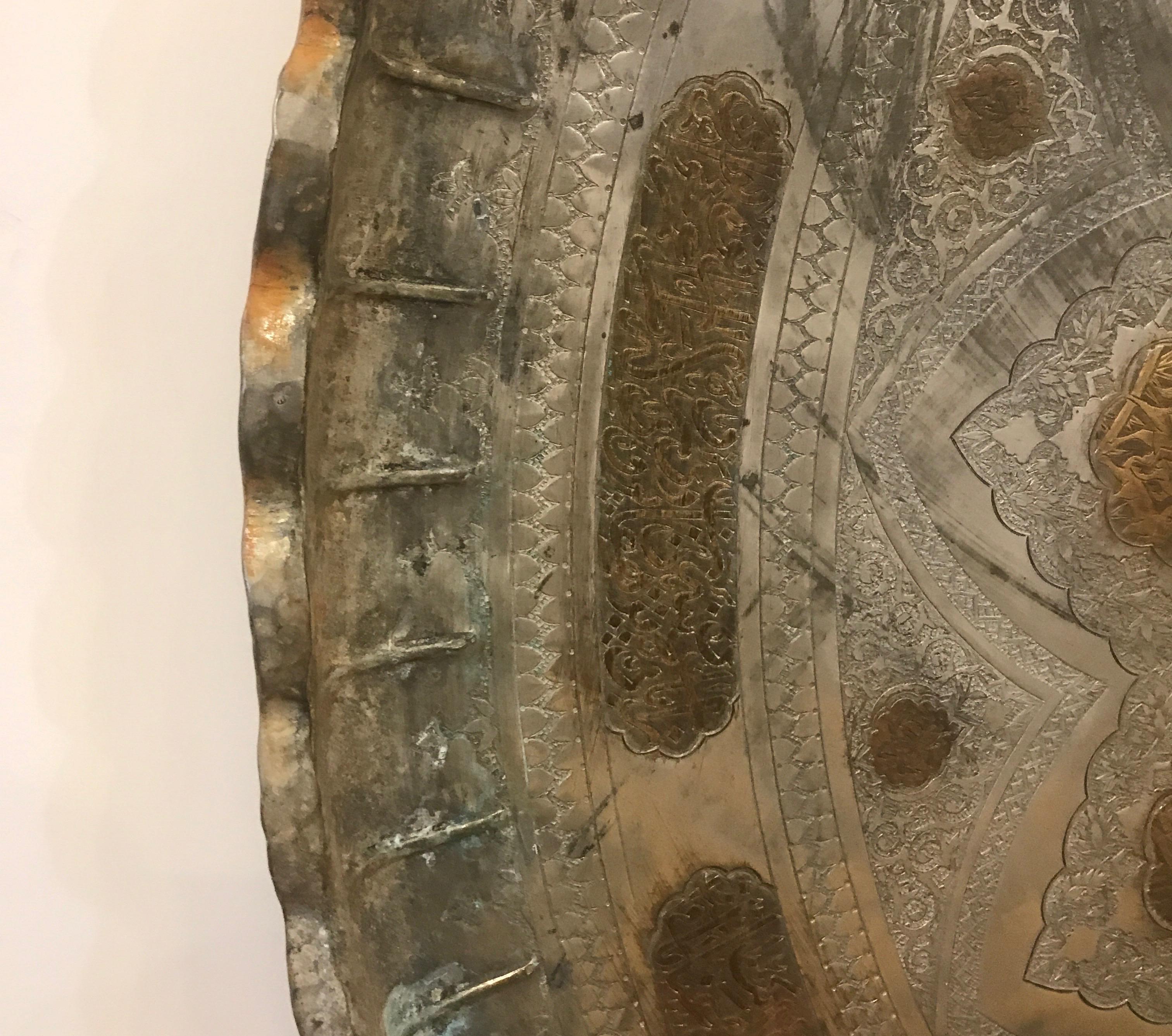 Un grand plateau en cuivre étamé aux détails complexes avec des panneaux et des décorations en écriture islamique. Cette pièce est d'origine et présente les signes habituels d'âge et d'utilisation. Mesures : 37 pouces de diamètre.