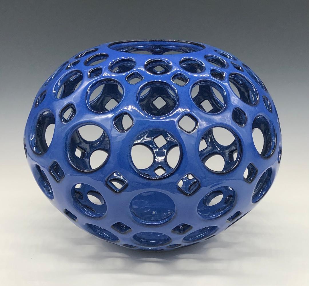 Inspired by Mid-Century Modern design, this piece is wheel thrown and hand pierced stoneware with a glossy cobalt glaze with black highlights. Smaller holes are created when the clay is still wet and then each hole is painstakingly enlarged and