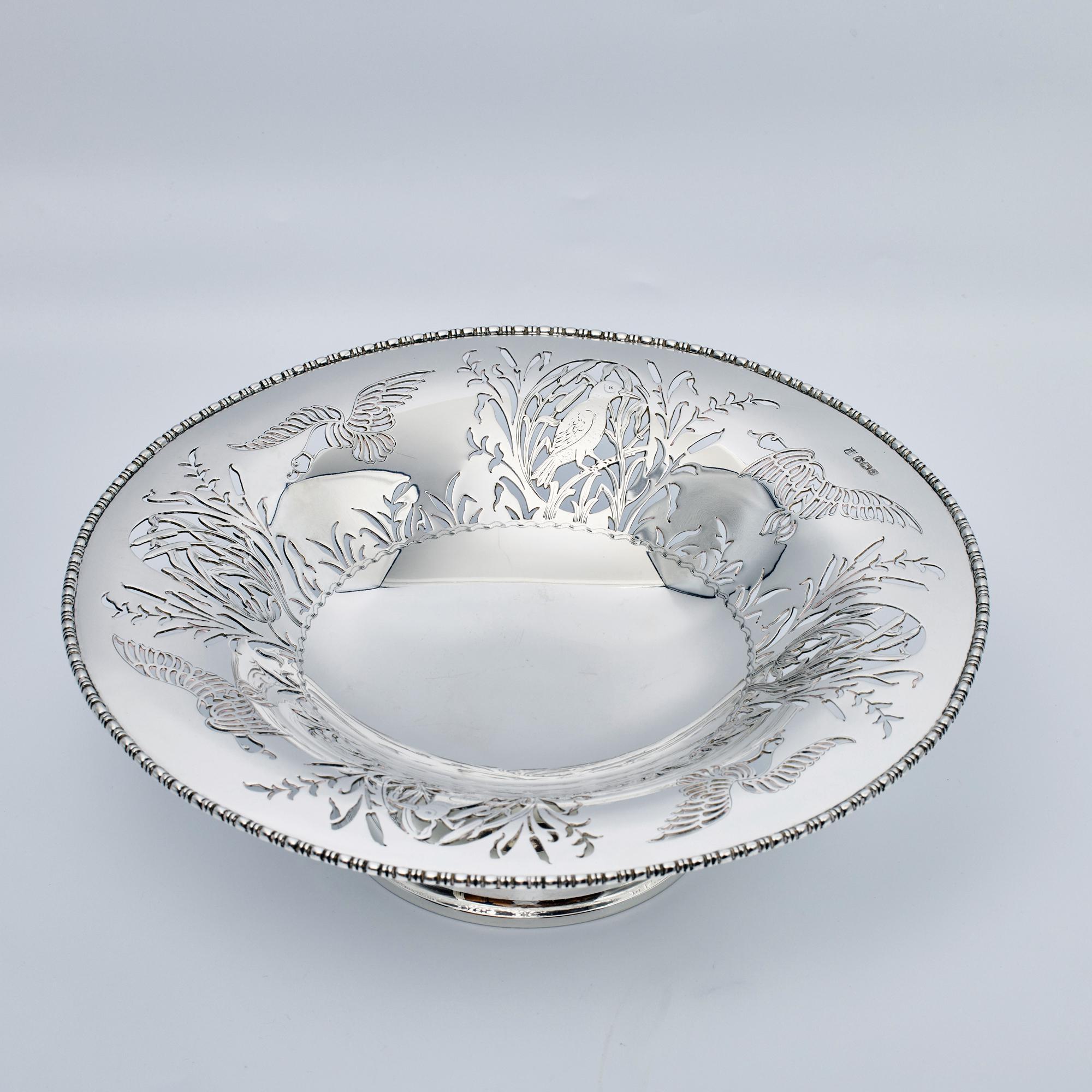 Shallow, decorative sterling silver saucer-like dish on a raised foot with a crisply hand-pierced body featuring flying ducks and birds among rushes, reeds and foliage. The rim is decorated with an applied bead and straight gadroon pattern