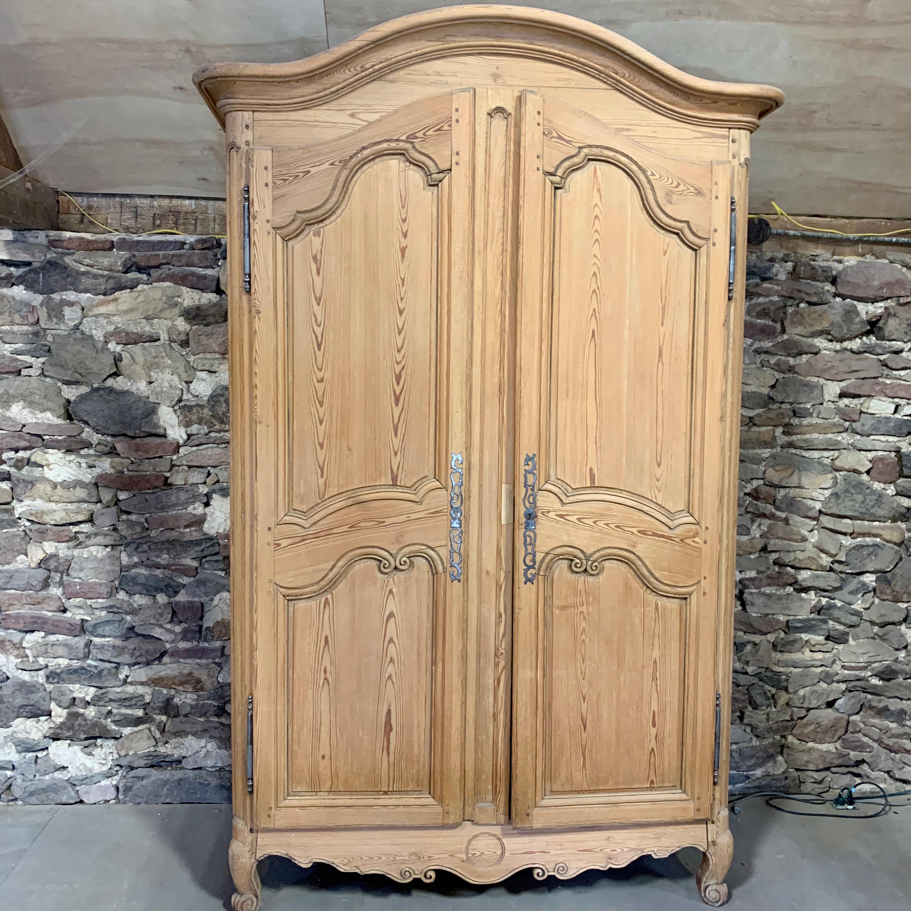 A large stripped pine Armoire, French Louis XV Period circa 1770, with an arched bonnet top, two large paneled doors on short cabriole legs. The interior has shelves (newer). Disassembles easily for transport.