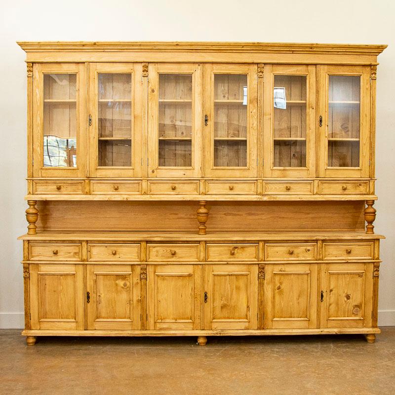 This striking large pine bookcase or display wall unit was newly made in Europe and breaks down into two large cabinets. The pine has a warm, inviting patina and country appeal thanks to a satin wax finish. The upper display section with six glass