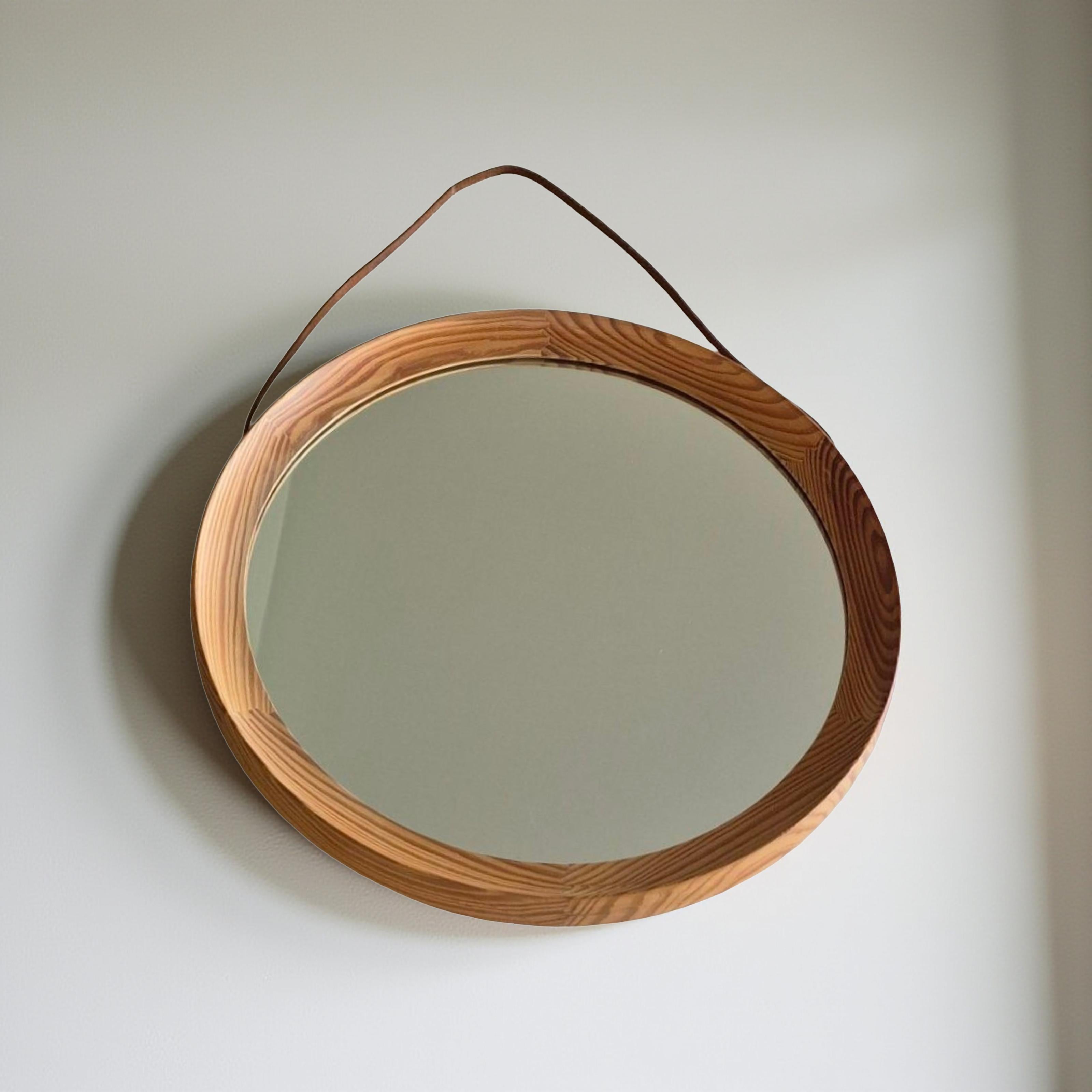 Grand miroir mural rond. Conçu par Uno & Östen Kristiansson pour Luxus Sweden dans les années 1960. Le cadre est en pin massif avec une menuiserie caractéristique. 

Le verre et le bois sont en bon état. Le bracelet en cuir d'origine est également