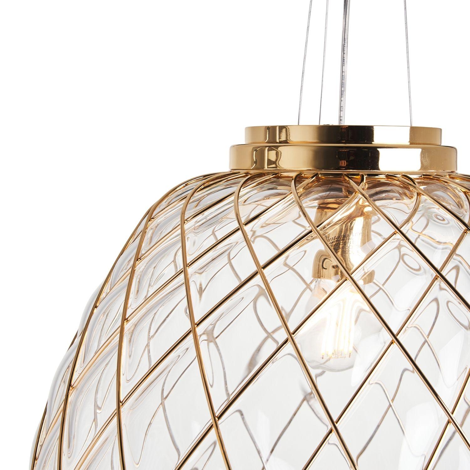 Grande lampada a sospensione 'Pinecone' in vetro trasparente e oro per Fontana Arte.

Disegnato da Paola Navone, il diffusore è sapientemente realizzato a mano con l'antica tecnica del vetro soffiato a gabbia. In questo caso, il vetraio soffia il