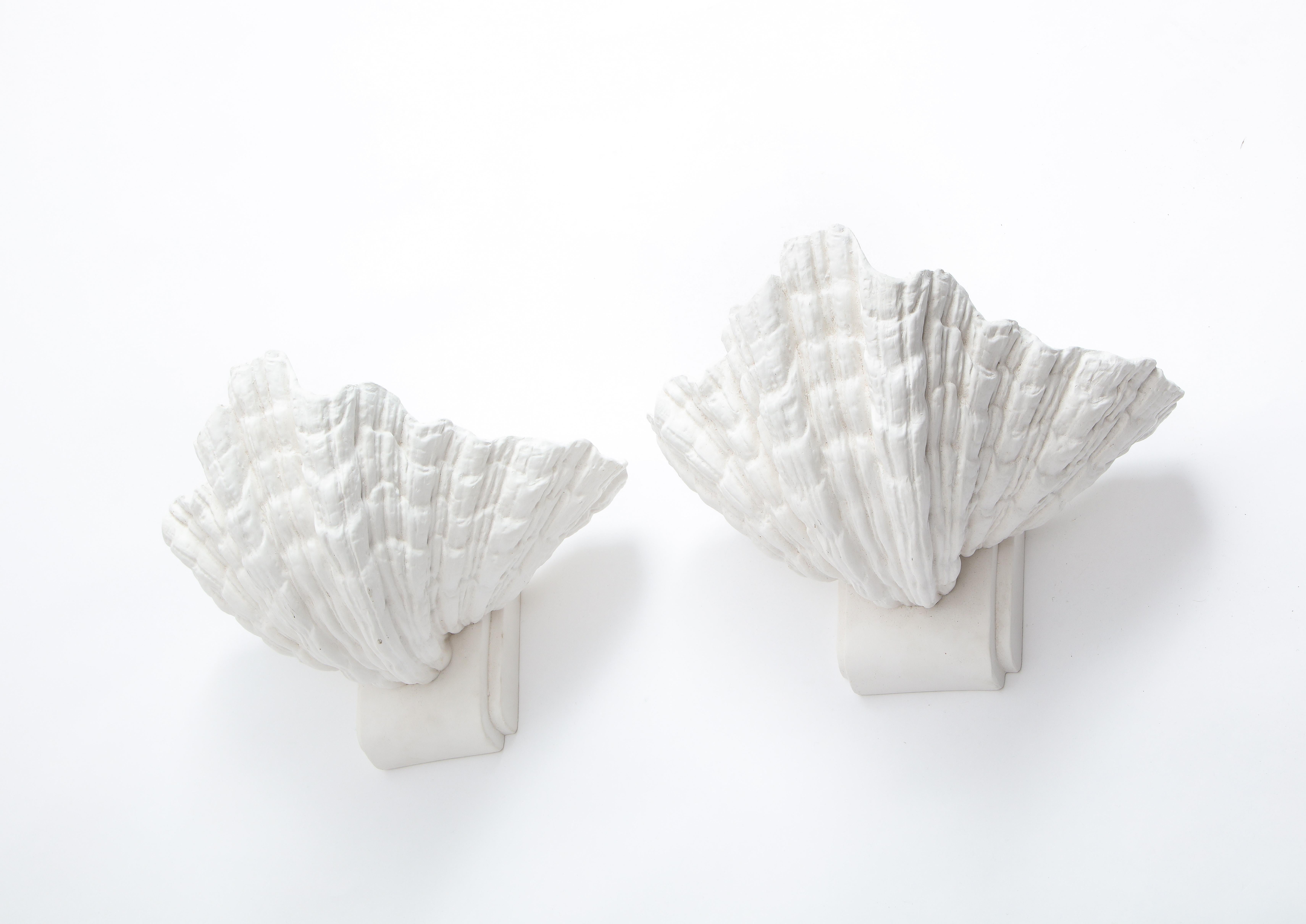 Large plaster sconces after Serge Roche, shaped like a giant seashell, hang on the wall via a hook in the back.