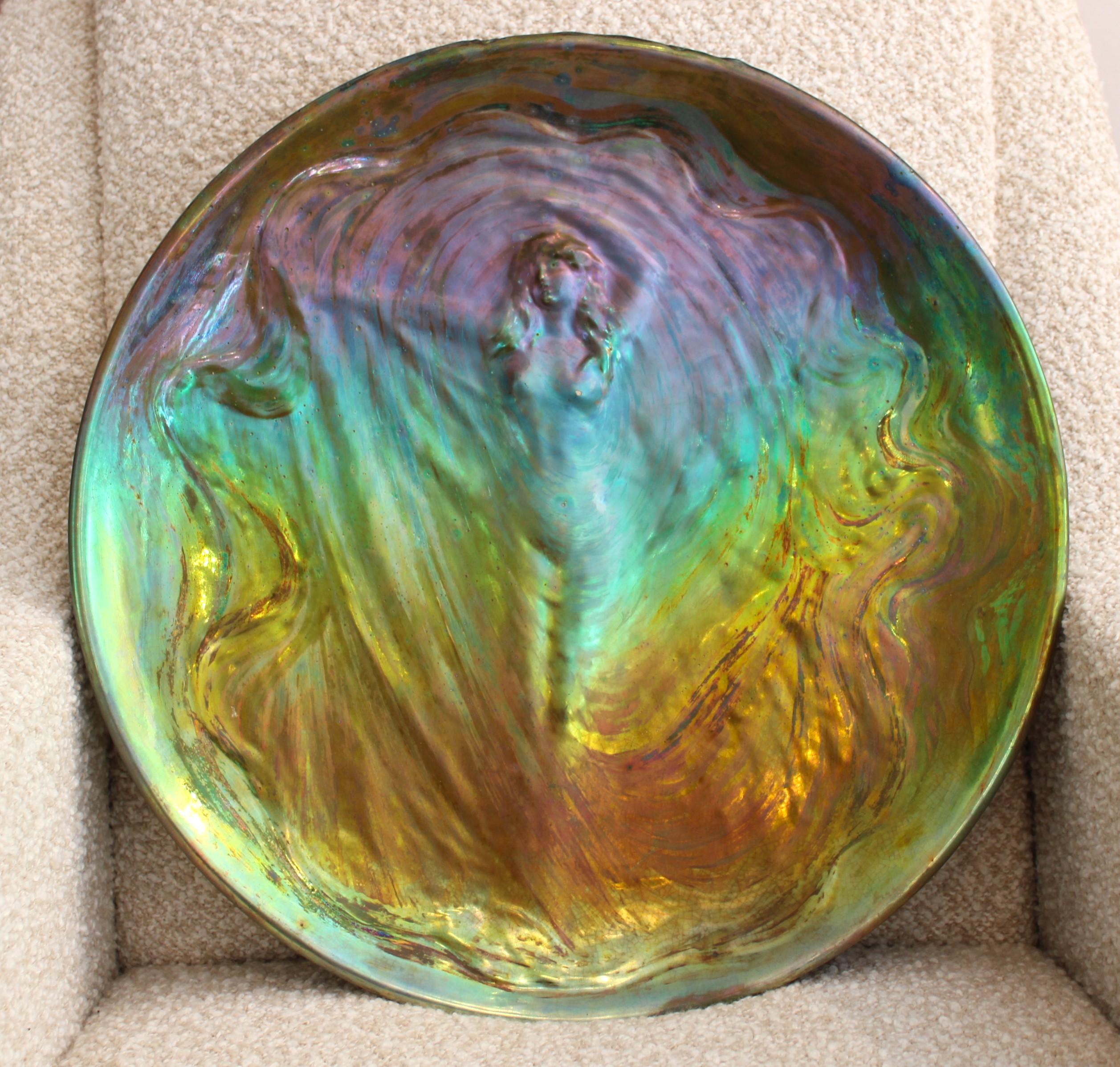 Clément MASSIER (1844-1917), large circular ceramic dish representing in bas-relief a large draped woman dancing
France, circa 1900 
Iridescent enamels with metallic 
Enameled and incised signatures “Clément Massier - Golfe Juan -A.M.”