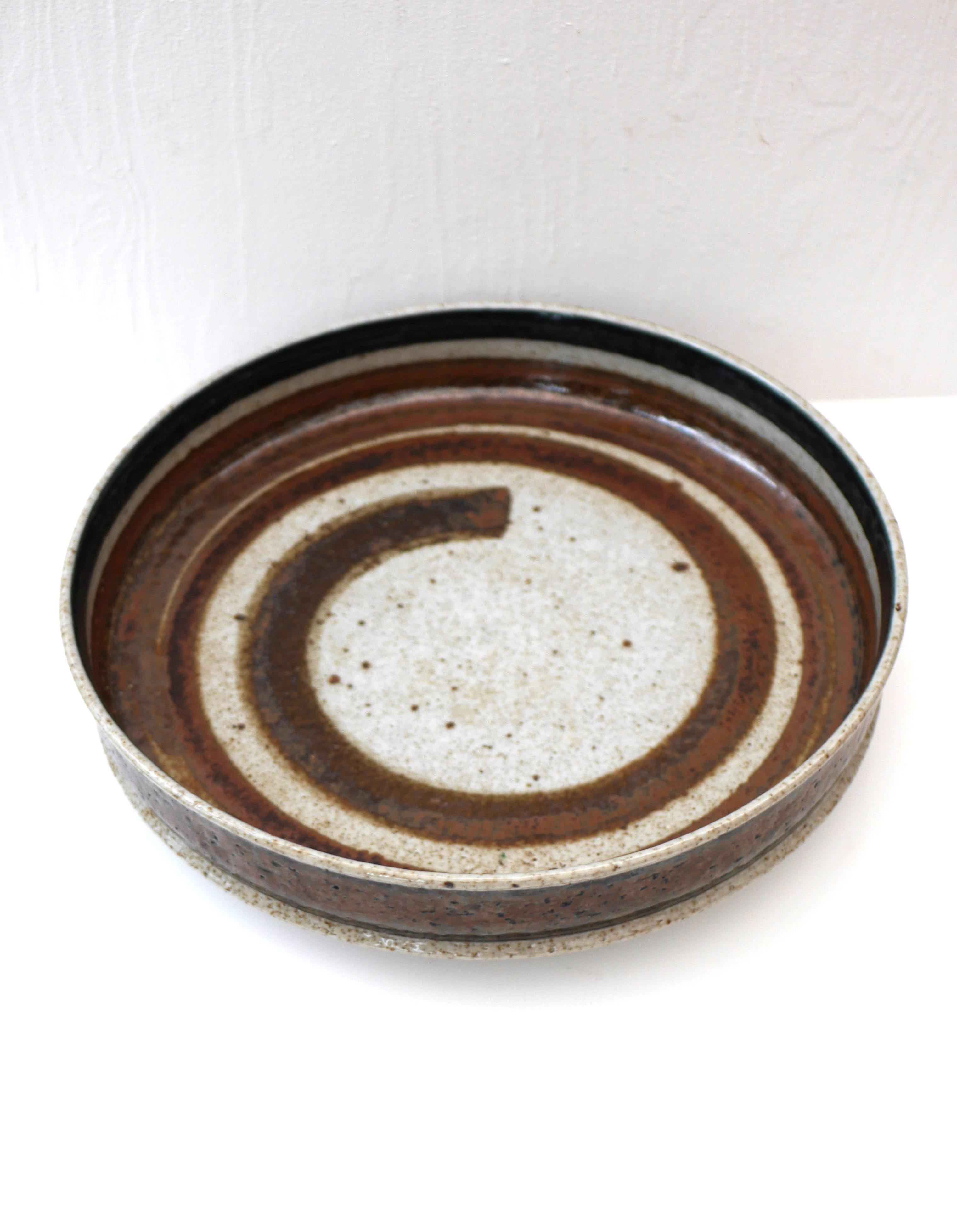A signed abstract art ceramic plate made by Inger Persson for Rörstrand, Sweden. This is a studio production and has an unusual pattern and technique with a swirl in a warm brown colour very smooth inside within combination with a dark blue outside