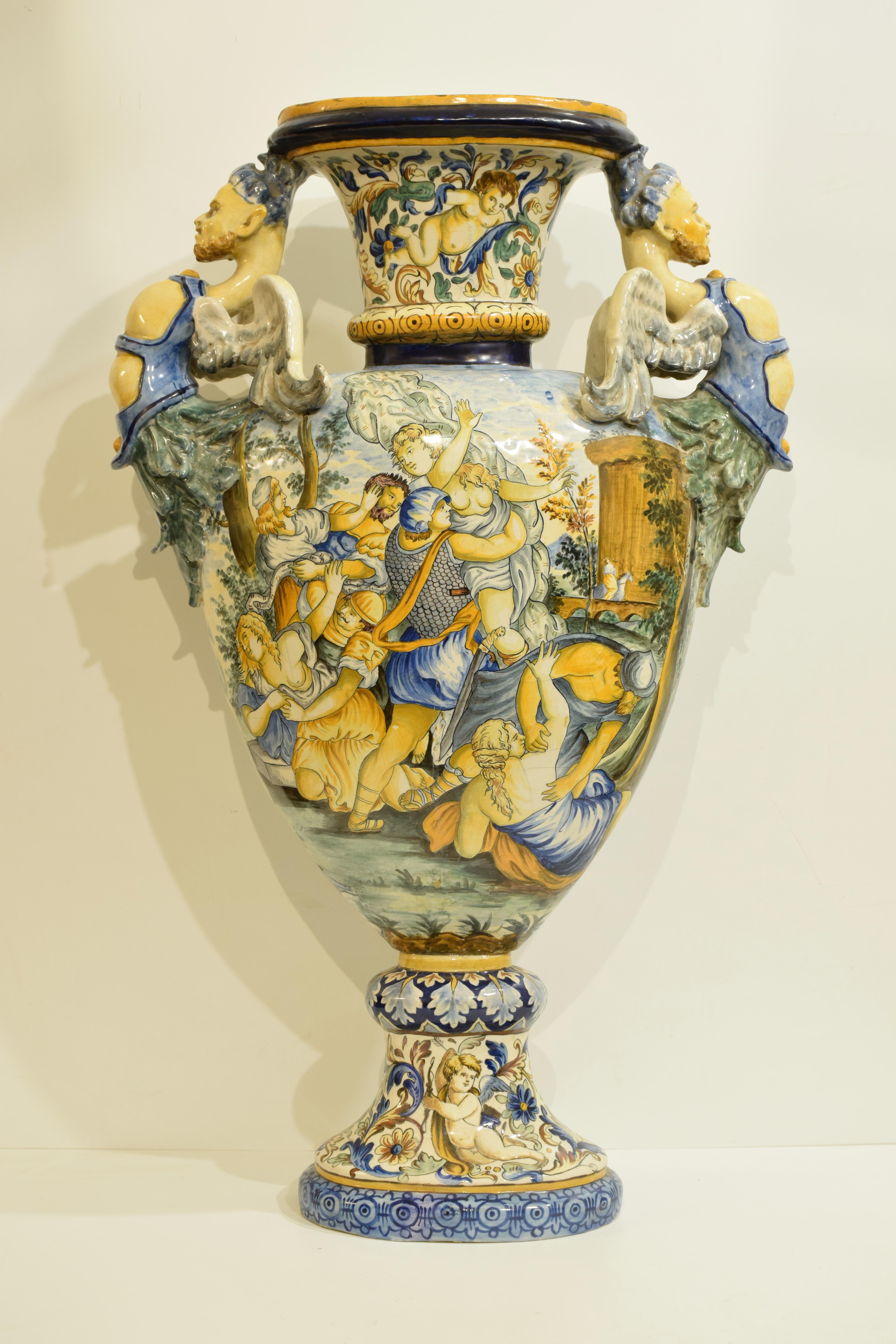 Imposant vase antique en majolique italienne, milieu du 19e siècle. Avec de très belles scènes classiques peintes à la main et des visages grotesques estampés sur les côtés de chaque poignée. Des vases similaires sont conservés dans des musées du