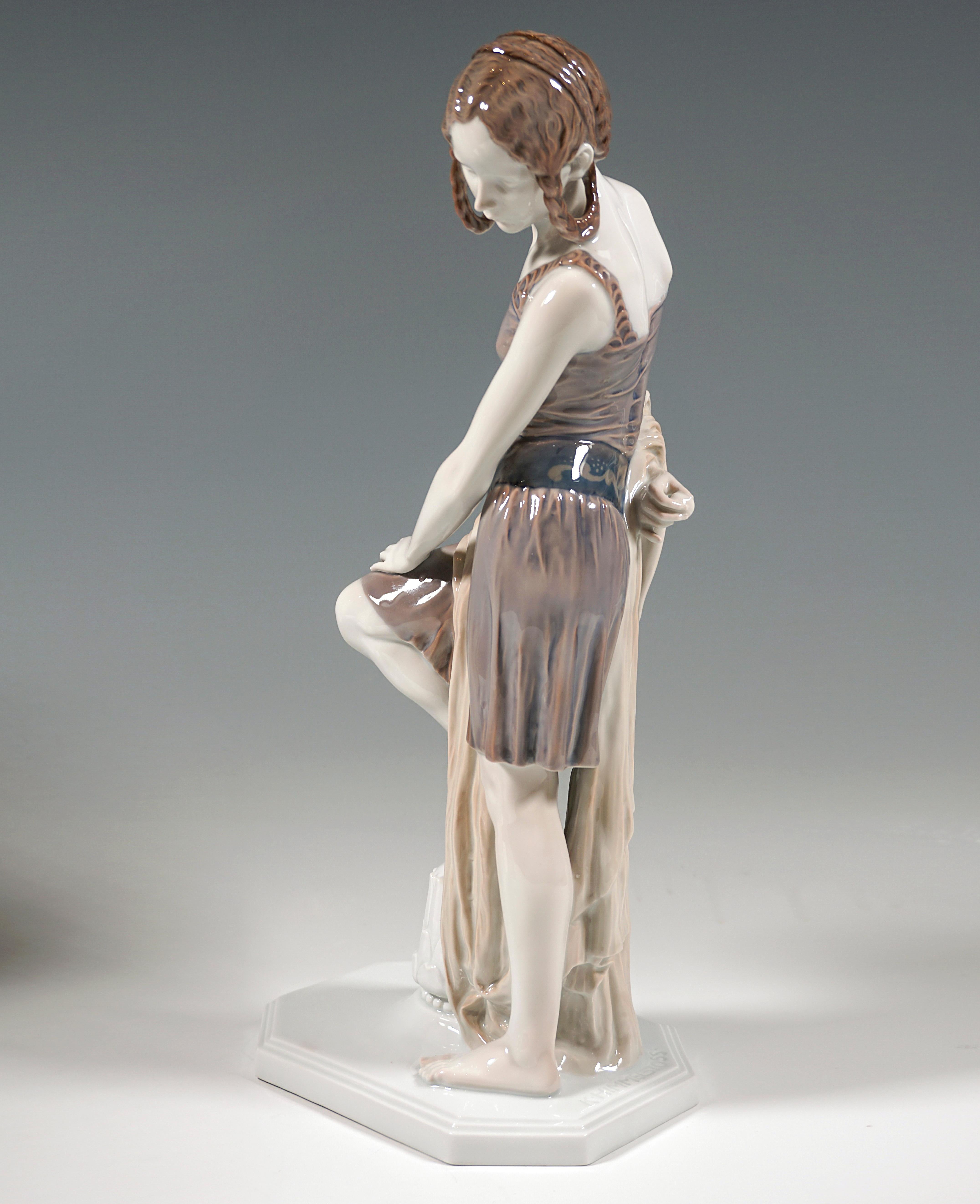 Ausgezeichnete seltene Rosenthal-Figur aus den 1920er Jahren:
Junge Frau in kurzem Trägerkleid mit kunstvoll geflochtenem und hochgestecktem Haar und 
verziertes Bauchband, Kopf nach links gedreht und zu Boden blickend, und 
ein langes, bis zum